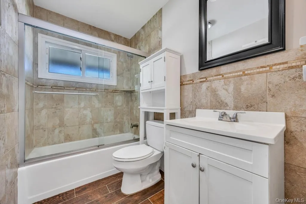 Bathroom featuring a glass-enclosed shower-tub combination, a sliding window, and floor-to-ceiling tiled walls Bathroom featuring a glass-enclosed shower-tub combination, a sliding window, and floor-to-ceiling tiled walls