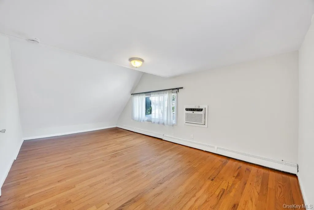 Room with wood-finish flooring, white walls, and an angled ceiling Room with wood-finish flooring, white walls, and an angled ceiling