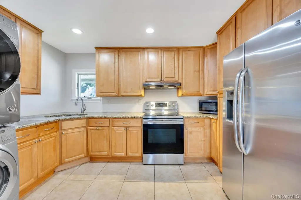 Kitchen featuring light wood-finish cabinetry, granite countertops, and stainless steel appliances including a refrigerator, range, and microwave Kitchen featuring light wood-finish cabinetry, granite countertops, and stainless steel appliances including a refrigerator, range, and microwave