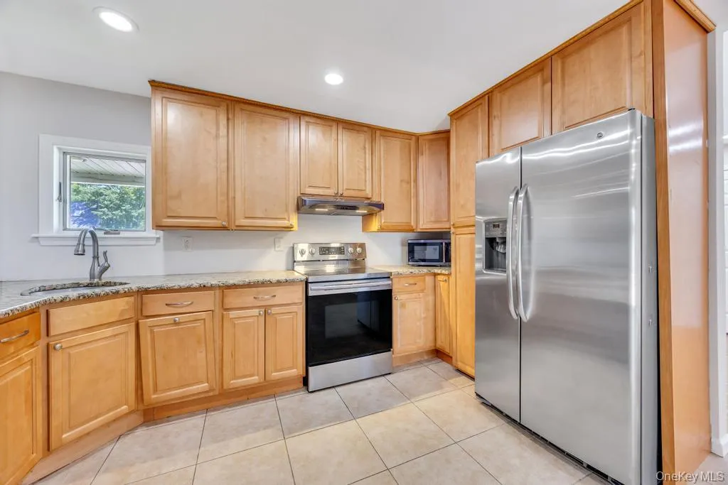 Kitchen featuring wood cabinetry, stainless steel appliances, granite countertops, and tiled flooring Kitchen featuring wood cabinetry, stainless steel appliances, granite countertops, and tiled flooring