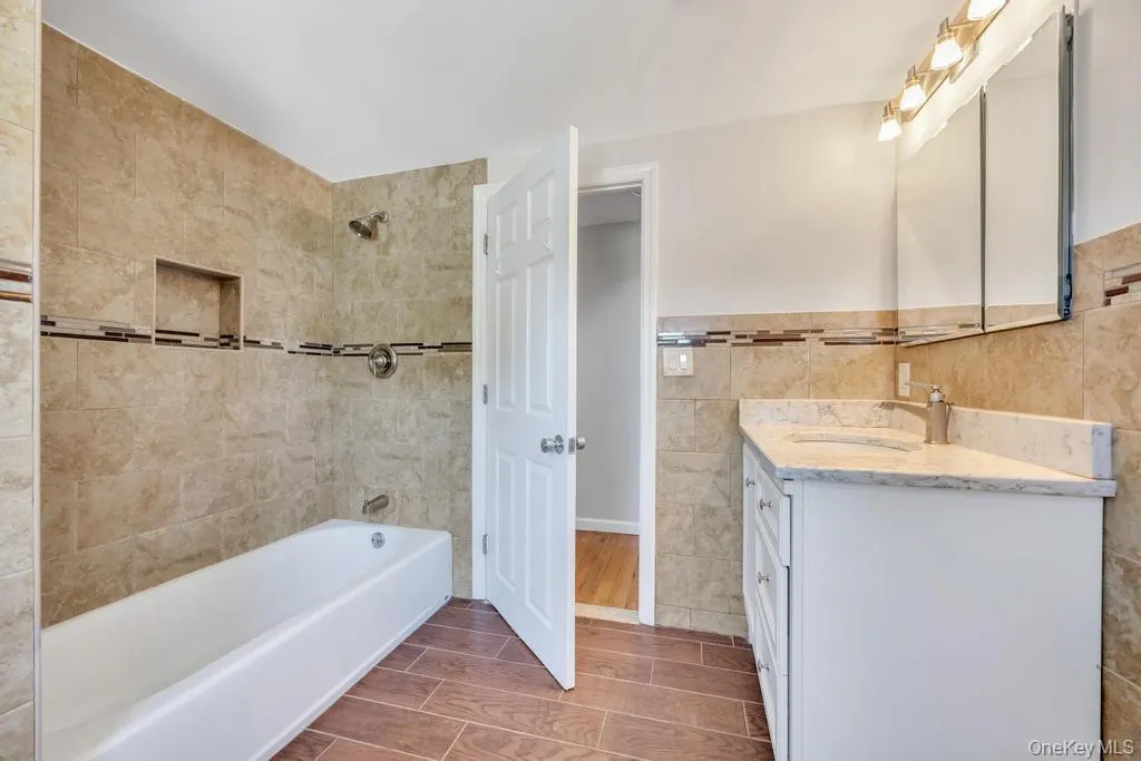 Bathroom with a white tub, shower featuring a tiled niche, and a vanity with a white countertop Bathroom with a white tub, shower featuring a tiled niche, and a vanity with a white countertop