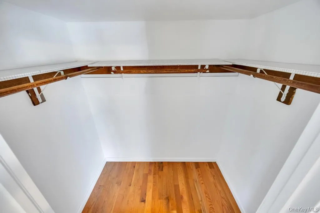 Walk-in closet featuring wood-finish flooring, white walls, and built-in wire shelving with wood rods Walk-in closet featuring wood-finish flooring, white walls, and built-in wire shelving with wood rods