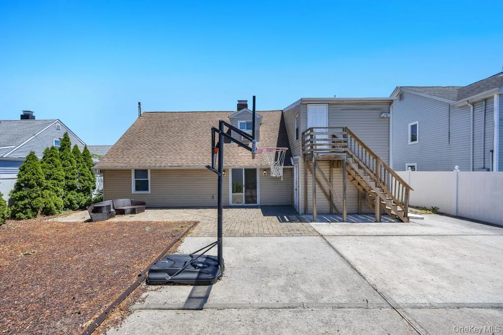 Rear exterior featuring a paver patio, concrete surface, and wood staircase Rear exterior featuring a paver patio, concrete surface, and wood staircase