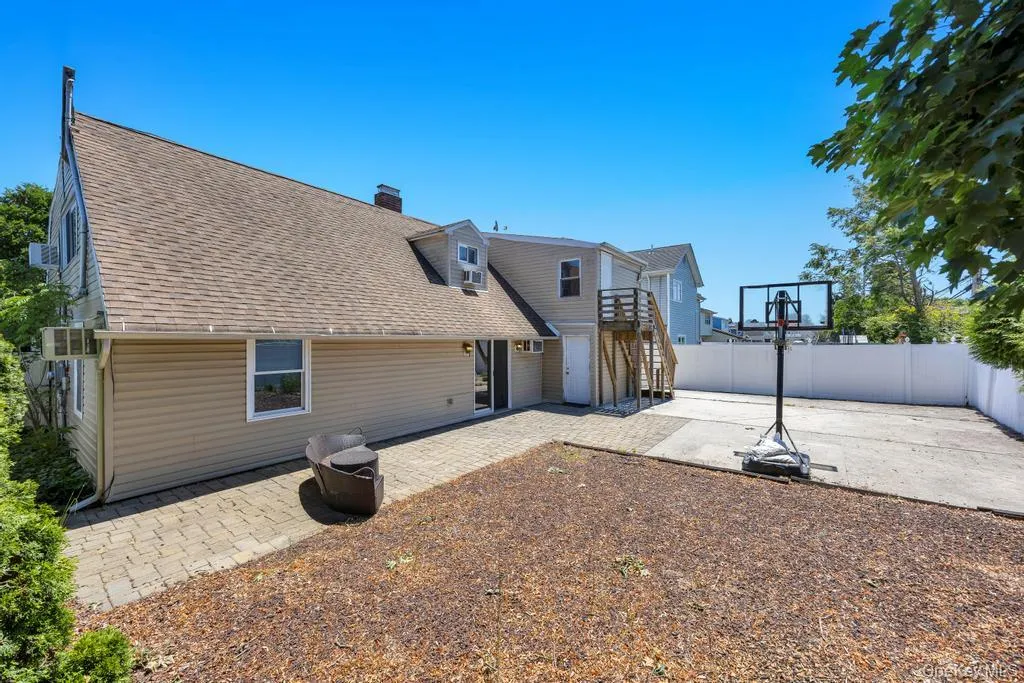 Rear exterior featuring tan siding, a gabled roofline, a second-story wooden deck with stairs, a patio with paver stones, and a concrete pad Rear exterior featuring tan siding, a gabled roofline, a second-story wooden deck with stairs, a patio with paver stones, and a concrete pad