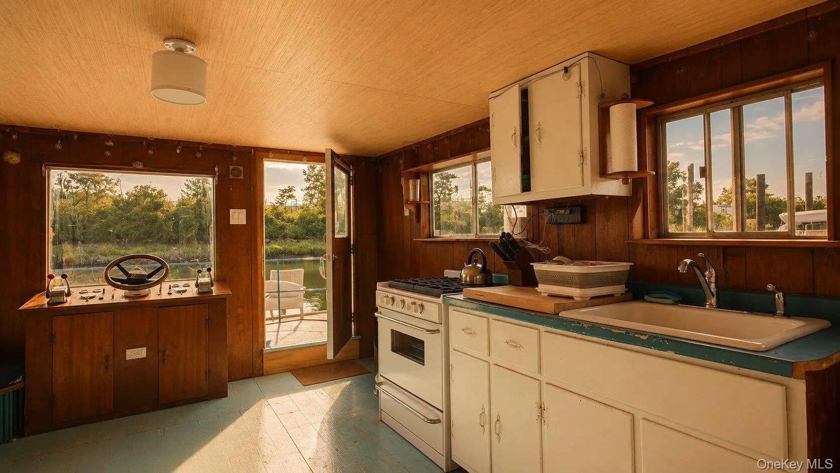 Interior cabin space featuring wood paneling, multiple windows, a steering station, and a kitchen area Interior cabin space featuring wood paneling, multiple windows, a steering station, and a kitchen area