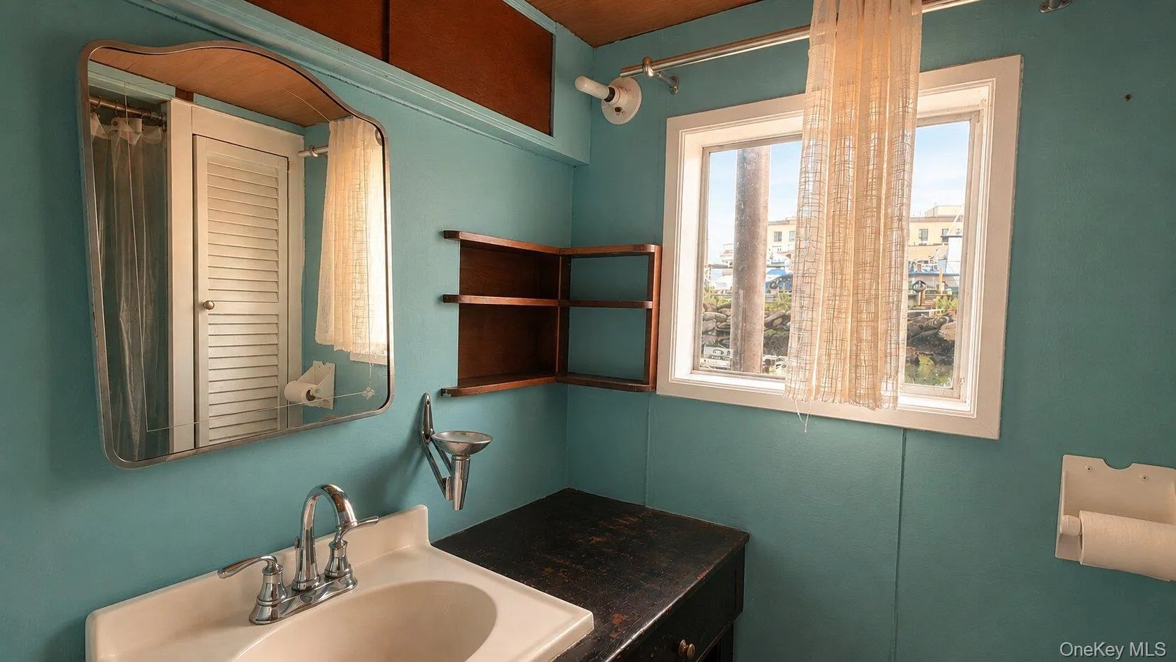 Bathroom featuring a single-pane window, corner shelving unit, wall-mounted mirror, and a vanity with an integrated sink Bathroom featuring a single-pane window, corner shelving unit, wall-mounted mirror, and a vanity with an integrated sink