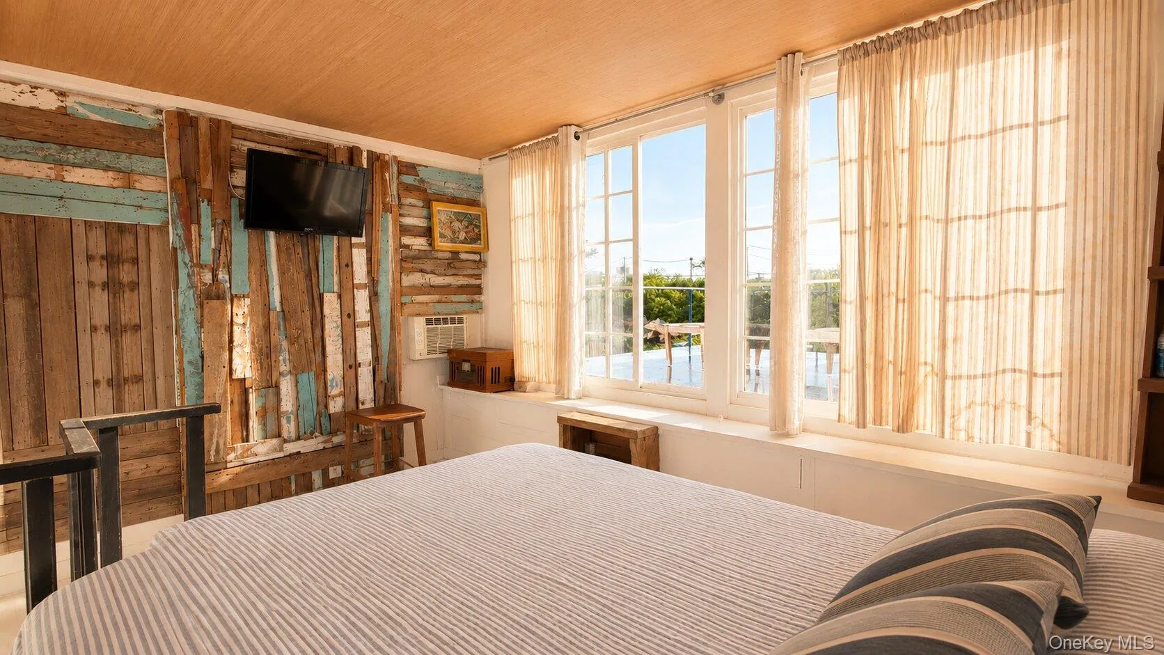 Reclaimed wood accent wall featuring a wall-mounted television and a window-mounted air conditioning unit Reclaimed wood accent wall featuring a wall-mounted television and a window-mounted air conditioning unit