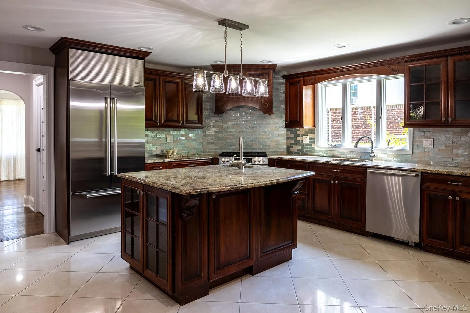 Kitchen featuring dark wood cabinetry, light granite countertops, stainless steel appliances, a center island with sink, and a tiled backsplash Kitchen featuring dark wood cabinetry, light granite countertops, stainless steel appliances, a center island with sink, and a tiled backsplash