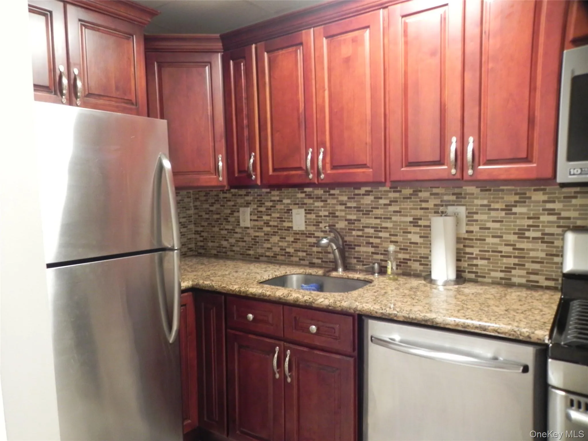 Kitchen with stainless steel appliances, dark brown cabinets, backsplash, and light stone countertops Kitchen with stainless steel appliances, dark brown cabinets, backsplash, and light stone countertops