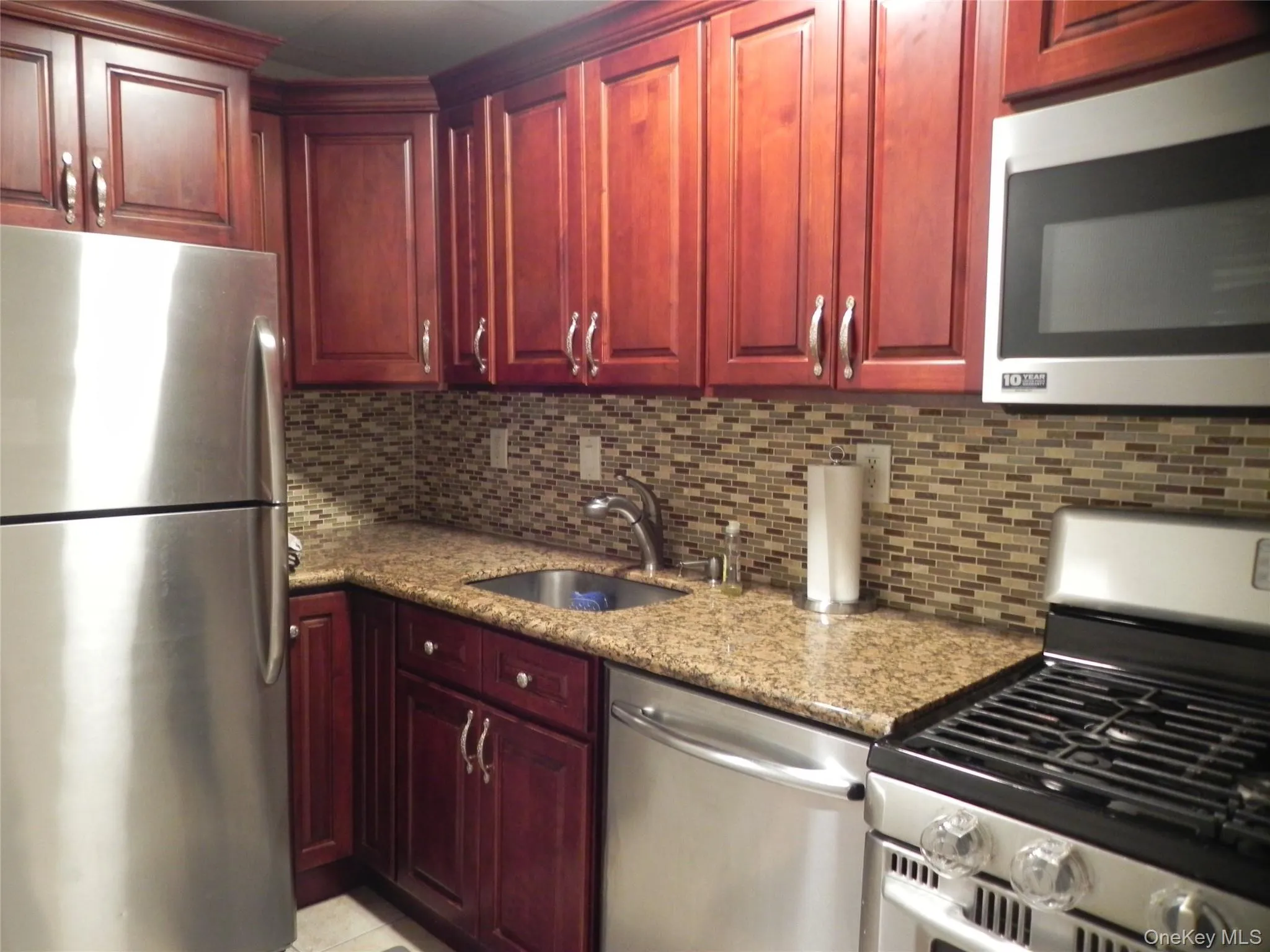 Kitchen featuring appliances with stainless steel finishes, dark brown cabinets, light stone counters, and decorative backsplash Kitchen featuring appliances with stainless steel finishes, dark brown cabinets, light stone counters, and decorative backsplash