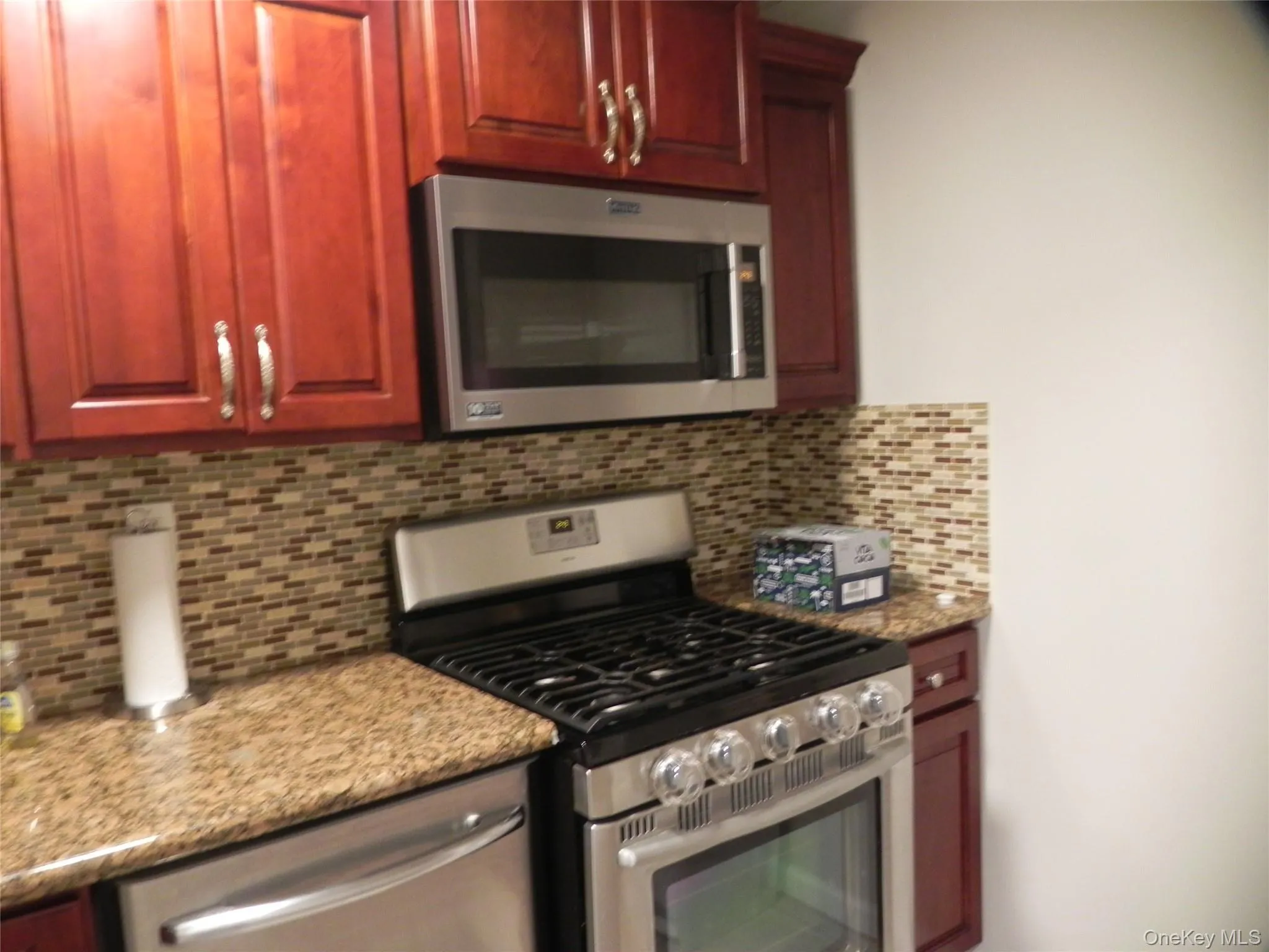 Kitchen featuring stainless steel appliances, backsplash, dark brown cabinets, and light stone countertops Kitchen featuring stainless steel appliances, backsplash, dark brown cabinets, and light stone countertops