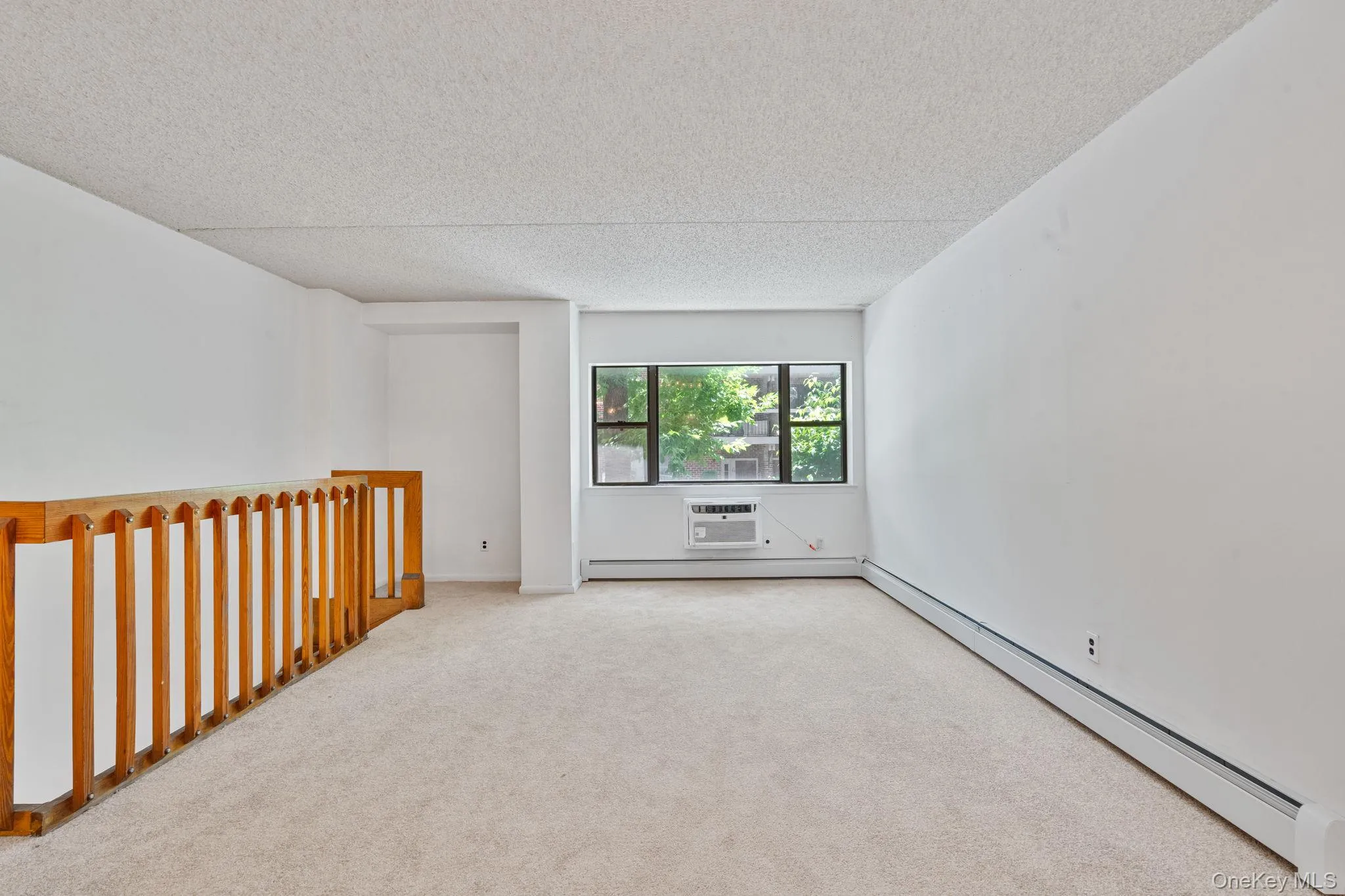 Carpeted room featuring a window with exterior foliage, white walls, and a window-mounted air conditioning unit Carpeted room featuring a window with exterior foliage, white walls, and a window-mounted air conditioning unit