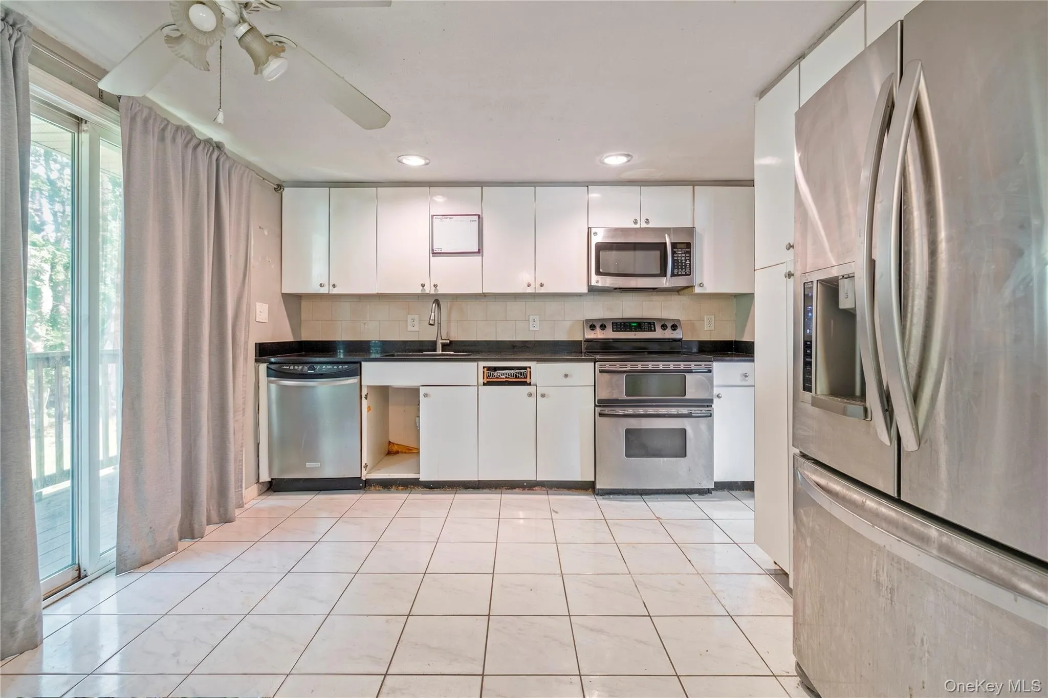 Kitchen featuring white cabinetry, stainless steel appliances, dark countertops, and tile flooring Kitchen featuring white cabinetry, stainless steel appliances, dark countertops, and tile flooring