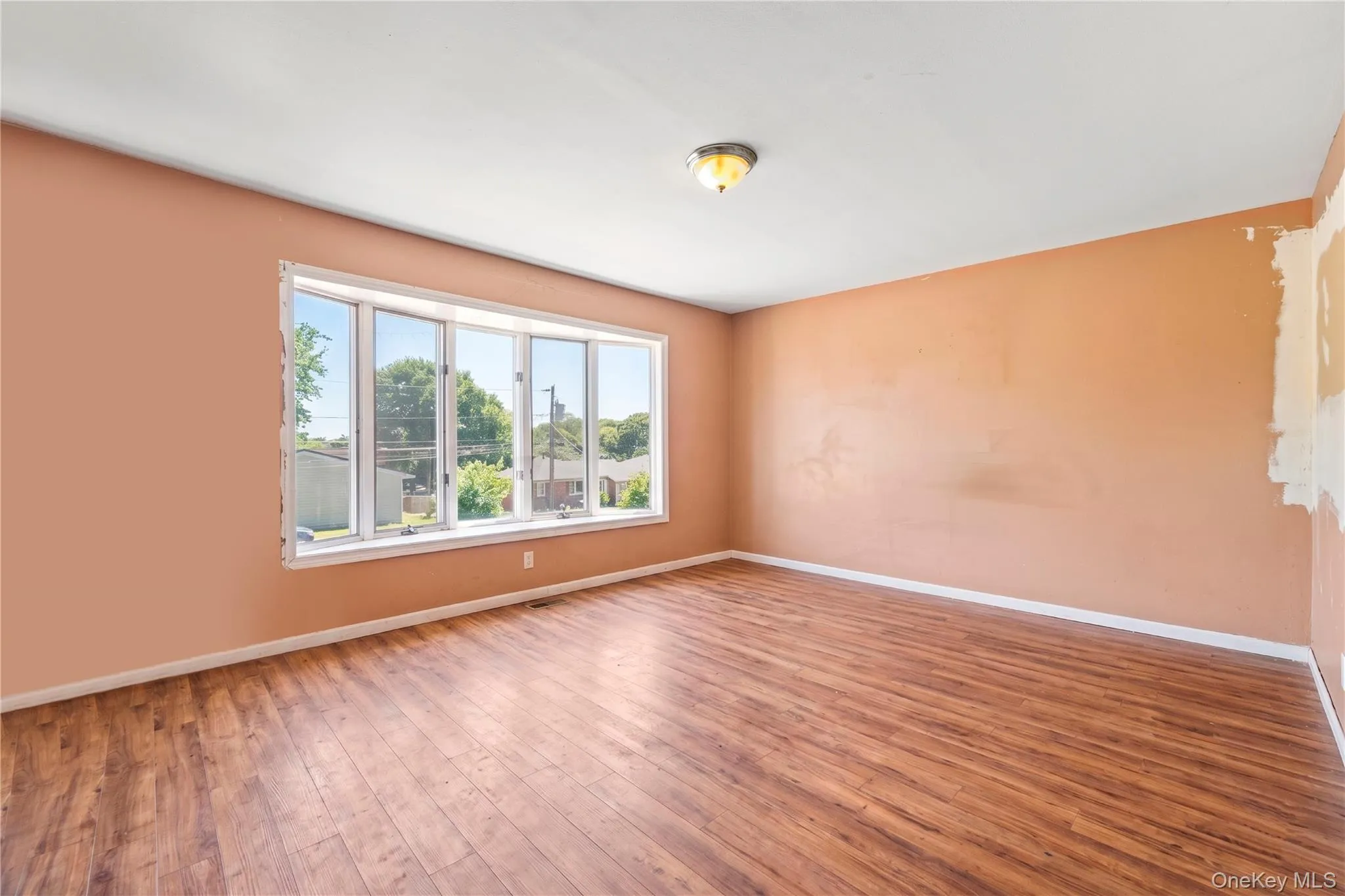 Spacious living room featuring wood-finish flooring and a large bay window Spacious living room featuring wood-finish flooring and a large bay window