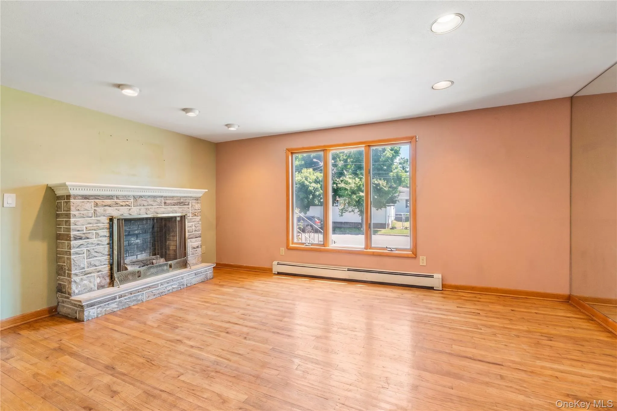 Spacious living room featuring wood-finish flooring, a stone-clad fireplace with a decorative mantel, and a large multi-pane window Spacious living room featuring wood-finish flooring, a stone-clad fireplace with a decorative mantel, and a large multi-pane window