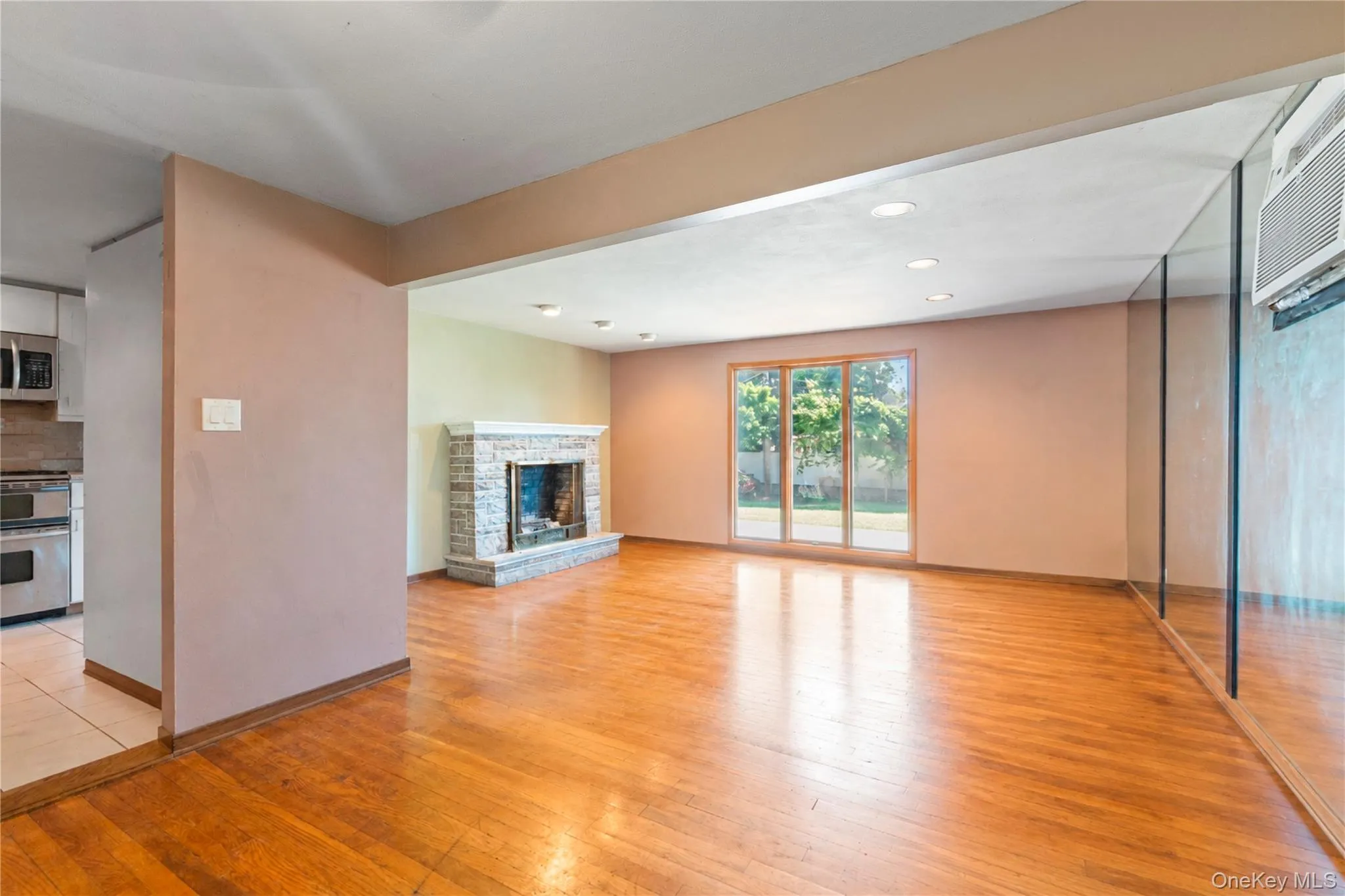 Spacious living area featuring wood-finish flooring, a stone-surround fireplace, recessed lighting, and sliding glass doors opening to the exterior Spacious living area featuring wood-finish flooring, a stone-surround fireplace, recessed lighting, and sliding glass doors opening to the exterior