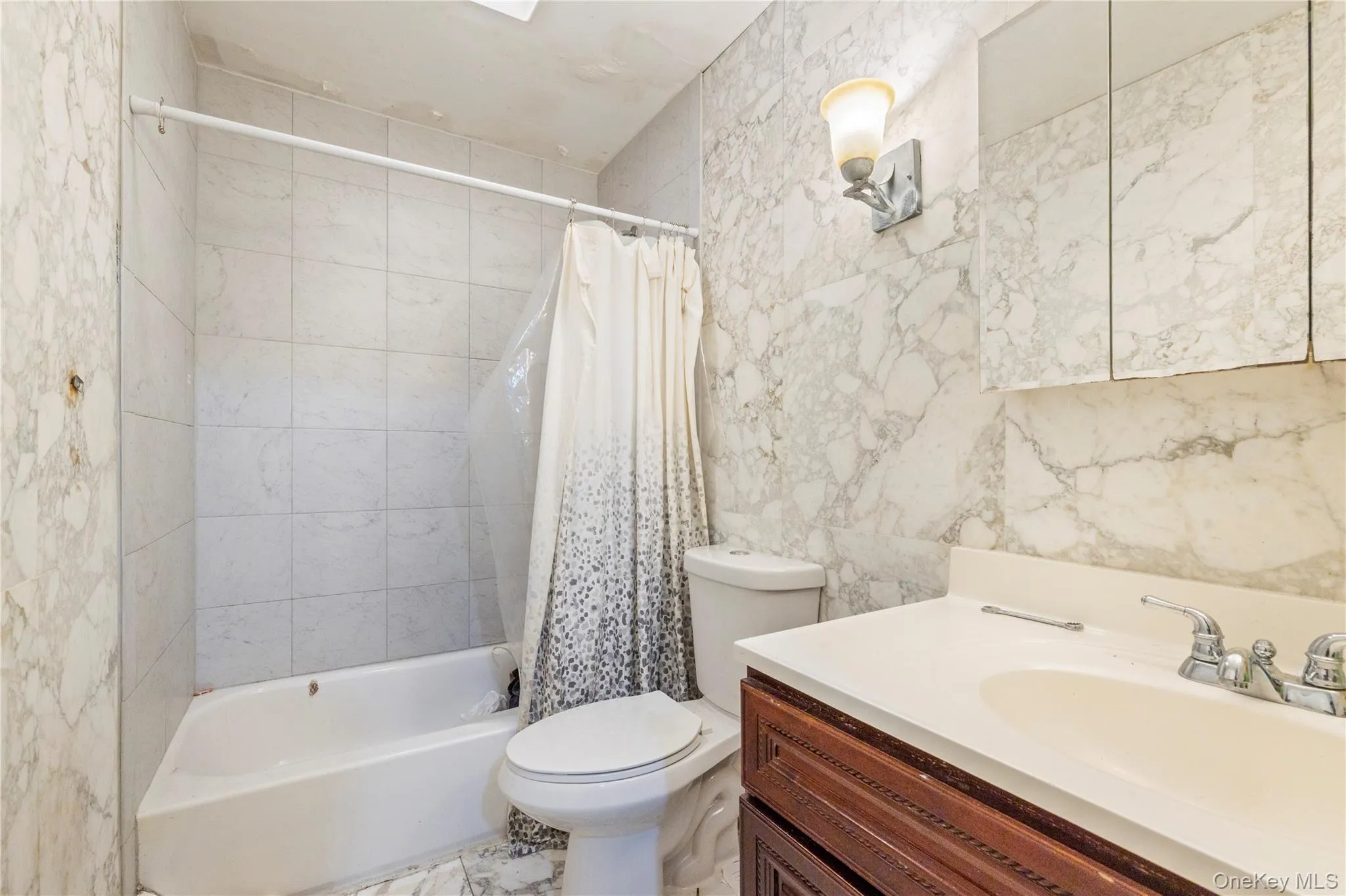 Bathroom featuring a bathtub with tiled surround, a toilet, a vanity with an integrated sink, a mirrored medicine cabinet, and wall-mounted lighting Bathroom featuring a bathtub with tiled surround, a toilet, a vanity with an integrated sink, a mirrored medicine cabinet, and wall-mounted lighting