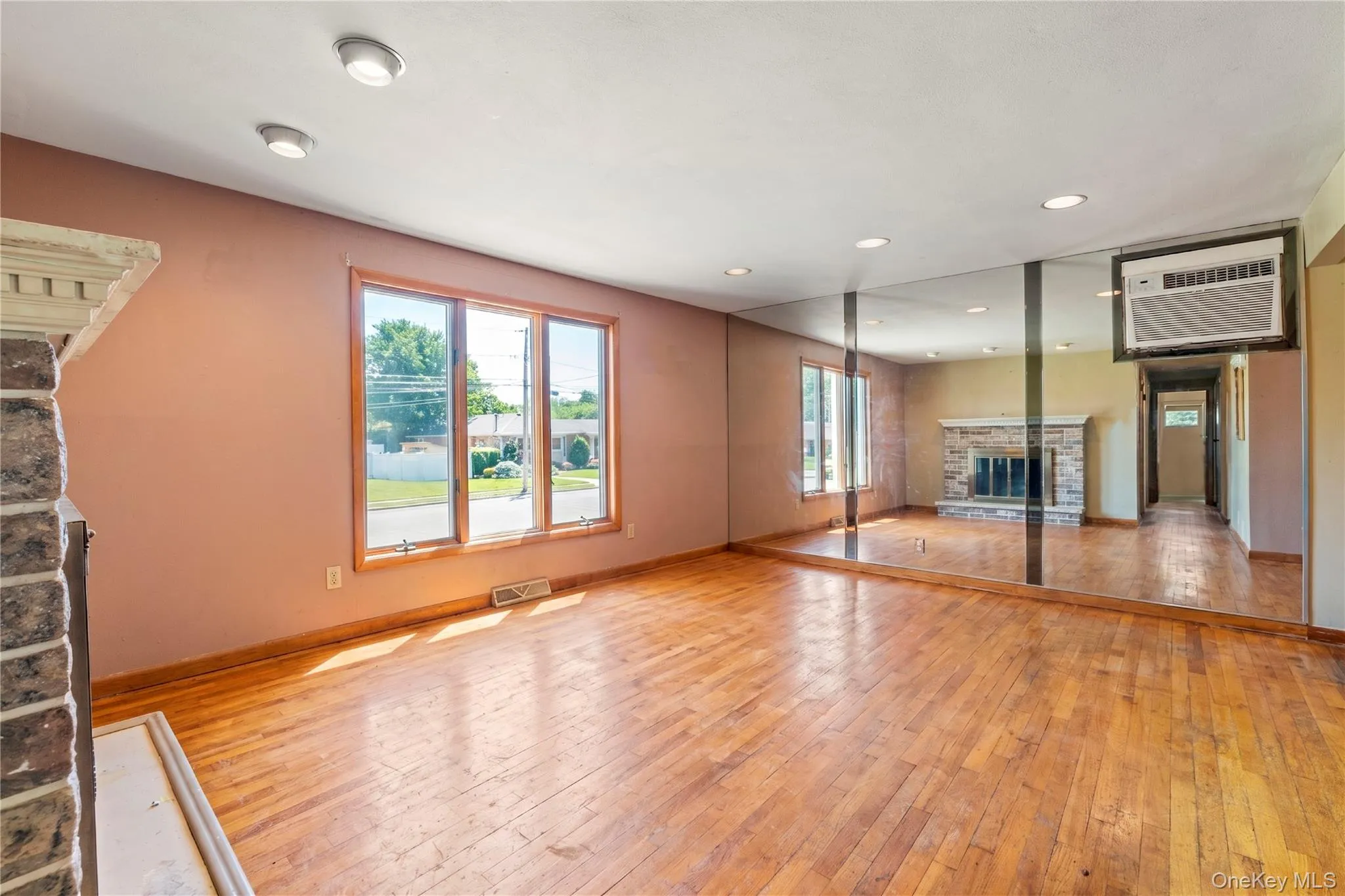 Living area featuring wood-finish flooring, a stone fireplace, large picture windows, recessed lighting, and a mirrored wall accent Living area featuring wood-finish flooring, a stone fireplace, large picture windows, recessed lighting, and a mirrored wall accent