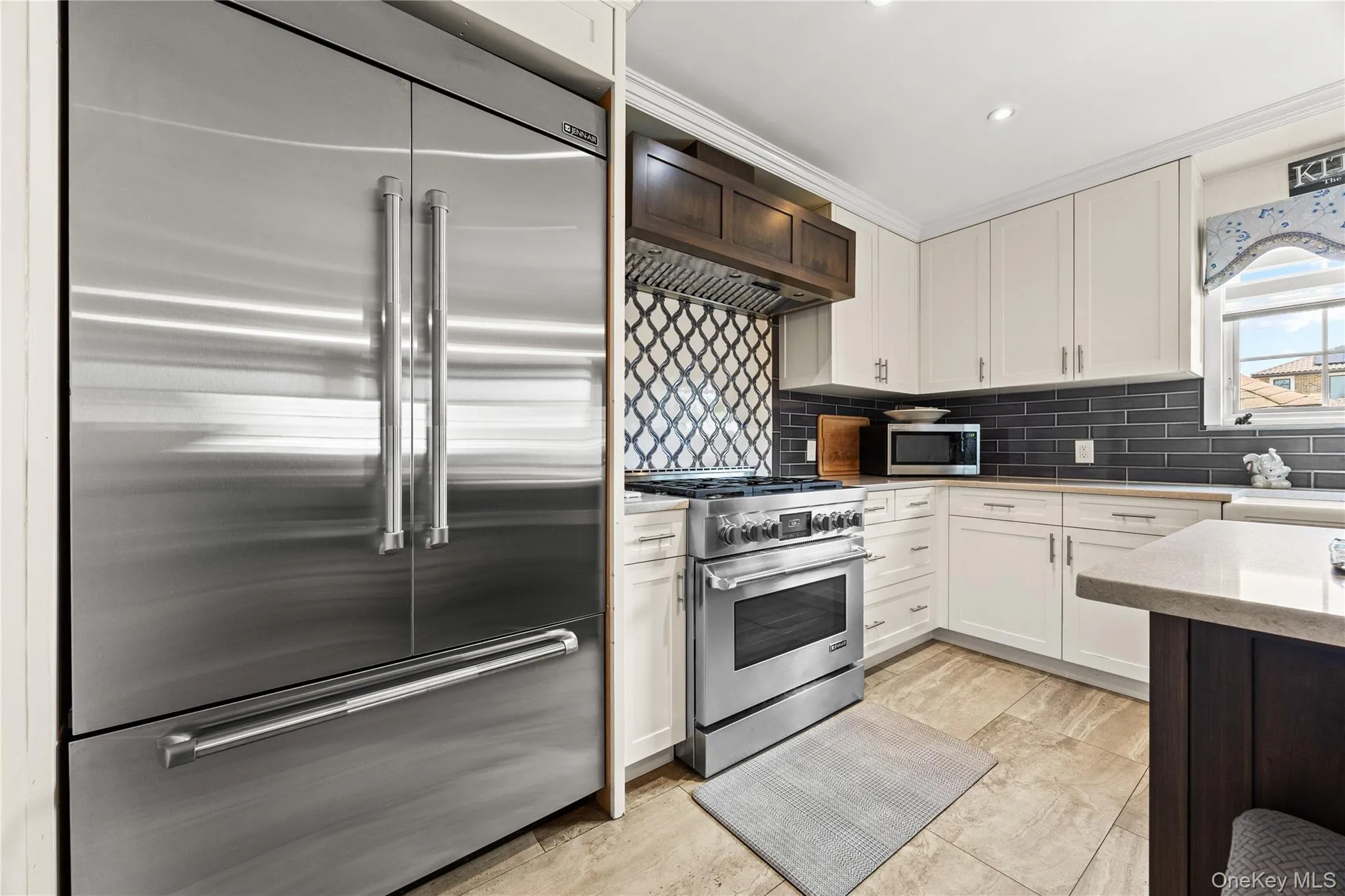 Gourmet kitchen featuring a built-in stainless steel refrigerator, stainless steel range with a custom wood hood, white shaker cabinetry, dark subway tile backsplash, and decorative arabesque tile accent Gourmet kitchen featuring a built-in stainless steel refrigerator, stainless steel range with a custom wood hood, white shaker cabinetry, dark subway tile backsplash, and decorative arabesque tile accent