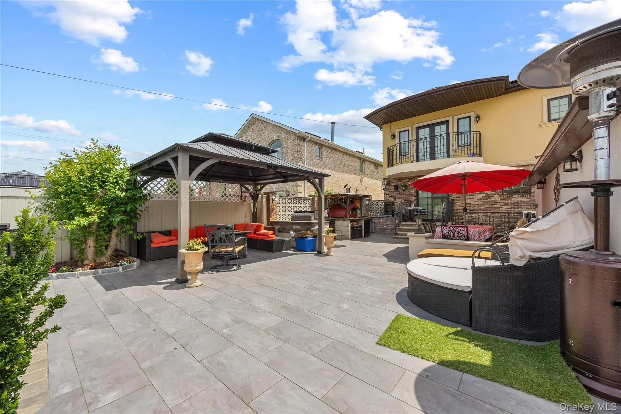 Expansive paved patio with a built-in gazebo, stone accent wall, and a curved balcony with iron railings Expansive paved patio with a built-in gazebo, stone accent wall, and a curved balcony with iron railings
