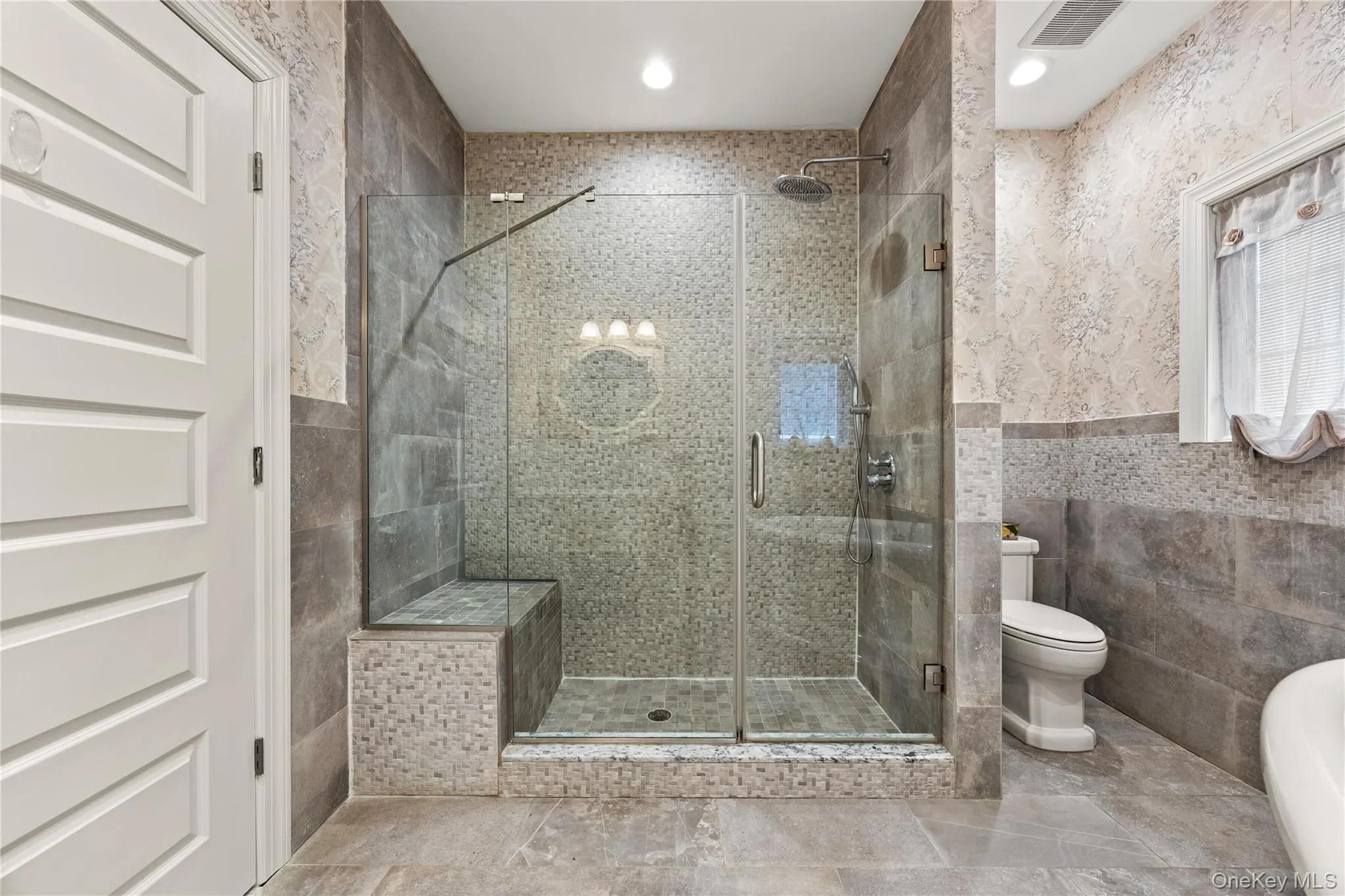 Spacious shower enclosure with glass doors, a built-in bench, and a rain shower head Spacious shower enclosure with glass doors, a built-in bench, and a rain shower head