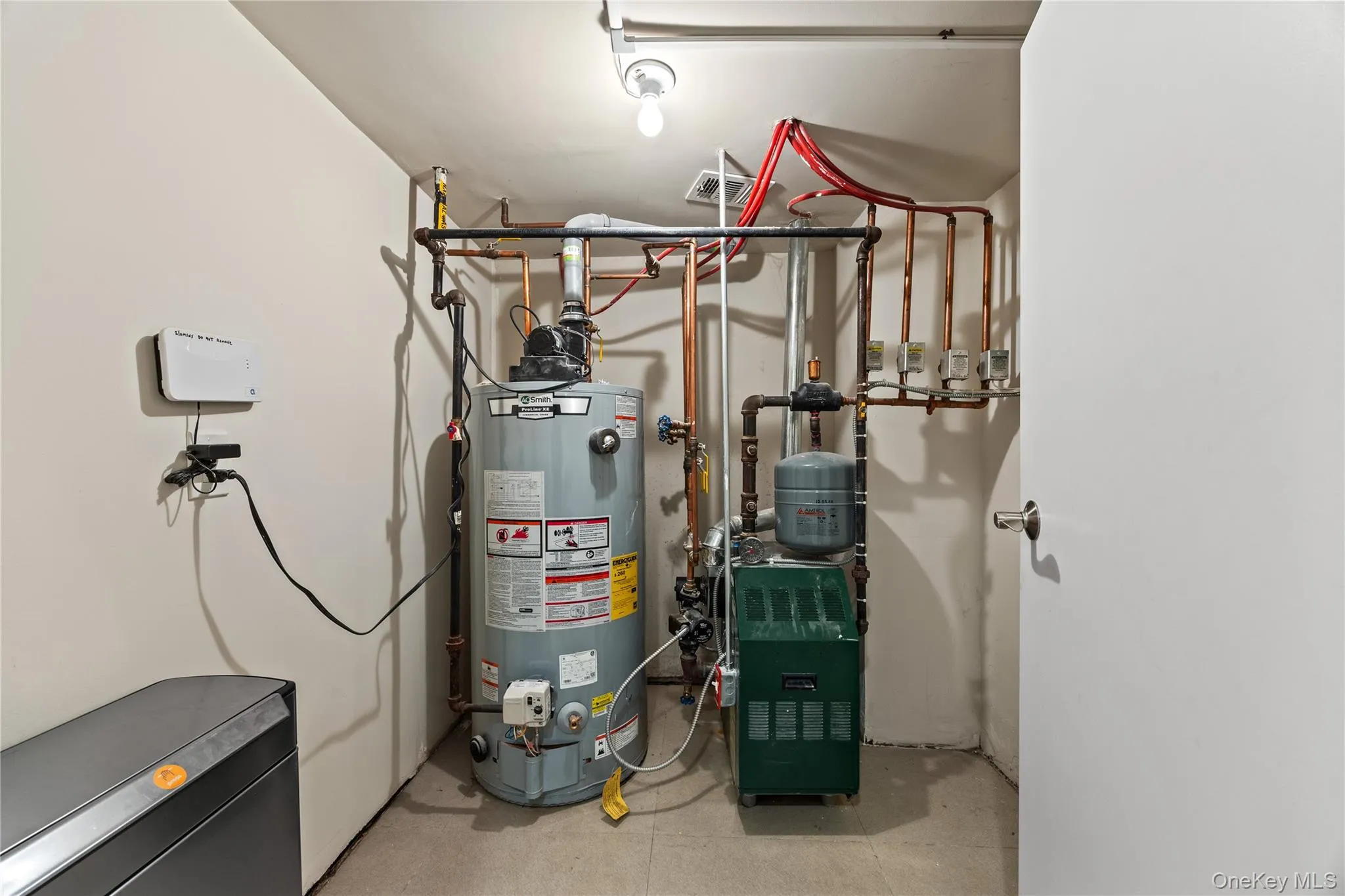 Dedicated utility space featuring a water heater, furnace, and water conditioning system with visible copper piping and modern white walls Dedicated utility space featuring a water heater, furnace, and water conditioning system with visible copper piping and modern white walls