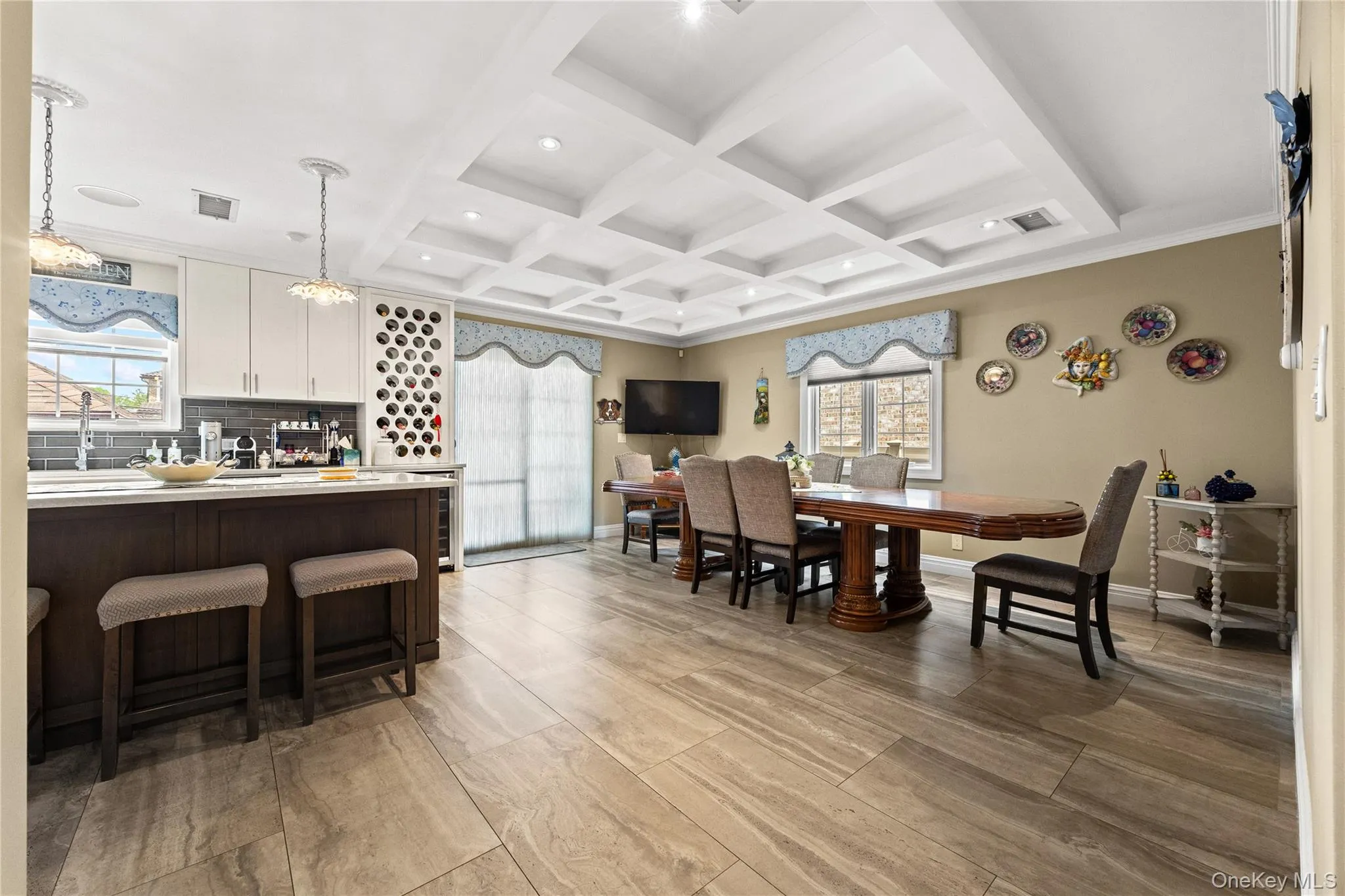 Open-concept living area featuring a coffered ceiling, wood-finish flooring, a kitchen island with white countertop, built-in wine storage, and a dining area Open-concept living area featuring a coffered ceiling, wood-finish flooring, a kitchen island with white countertop, built-in wine storage, and a dining area