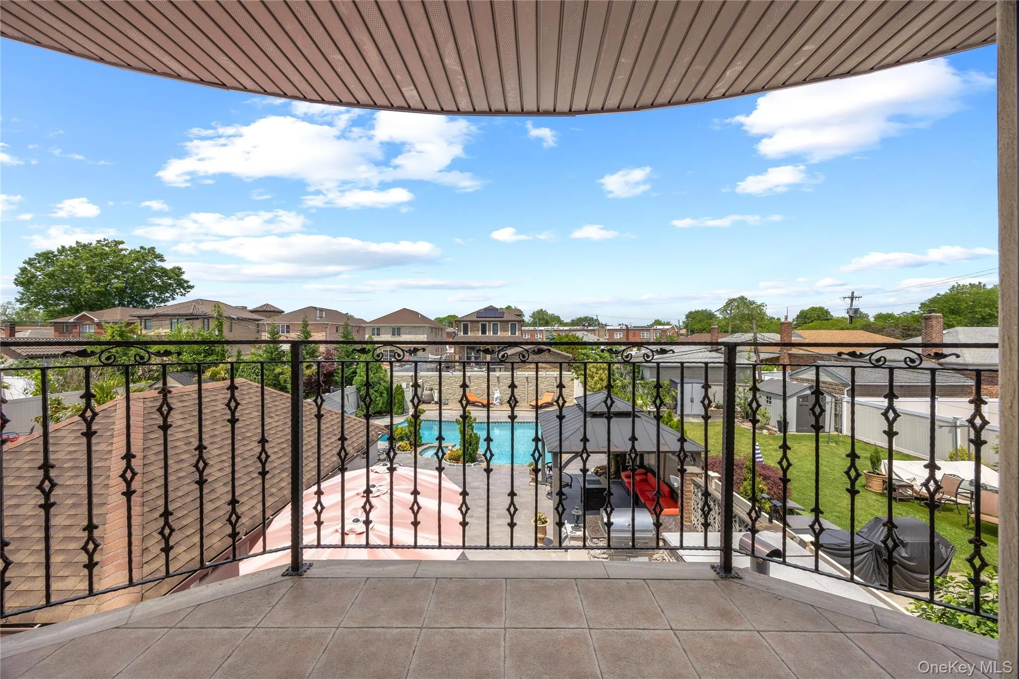 Balcony featuring decorative wrought iron railing and tile flooring, overlooking a backyard with a swimming pool and covered gazebo Balcony featuring decorative wrought iron railing and tile flooring, overlooking a backyard with a swimming pool and covered gazebo