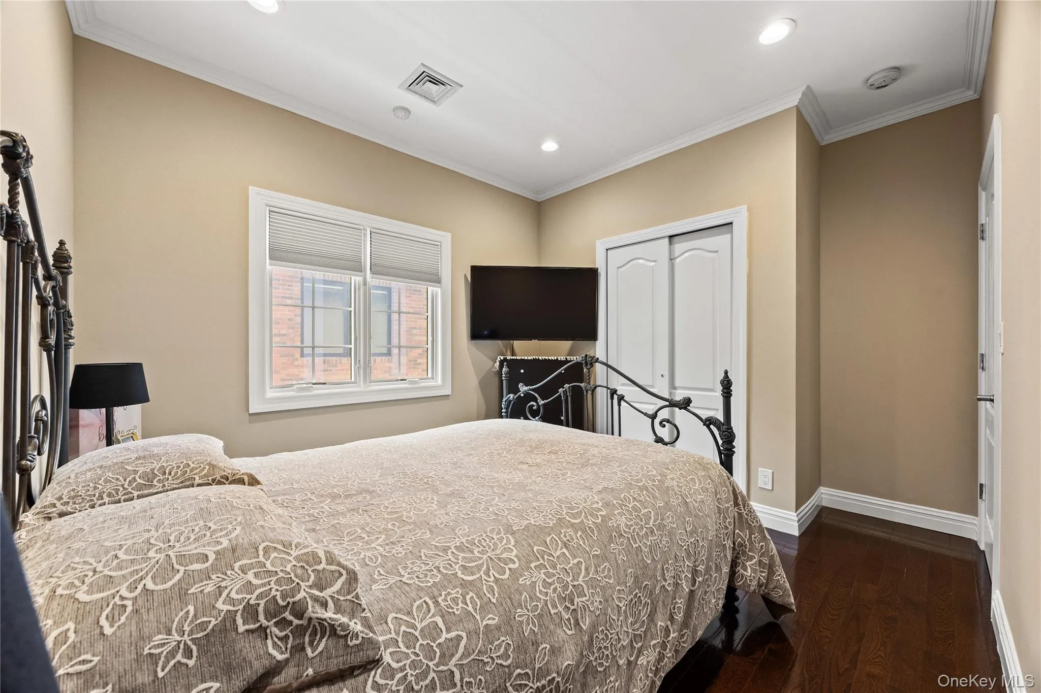 Recessed lighting illuminates this room, featuring wood-finish flooring, a double window with blinds, and white crown molding Recessed lighting illuminates this room, featuring wood-finish flooring, a double window with blinds, and white crown molding