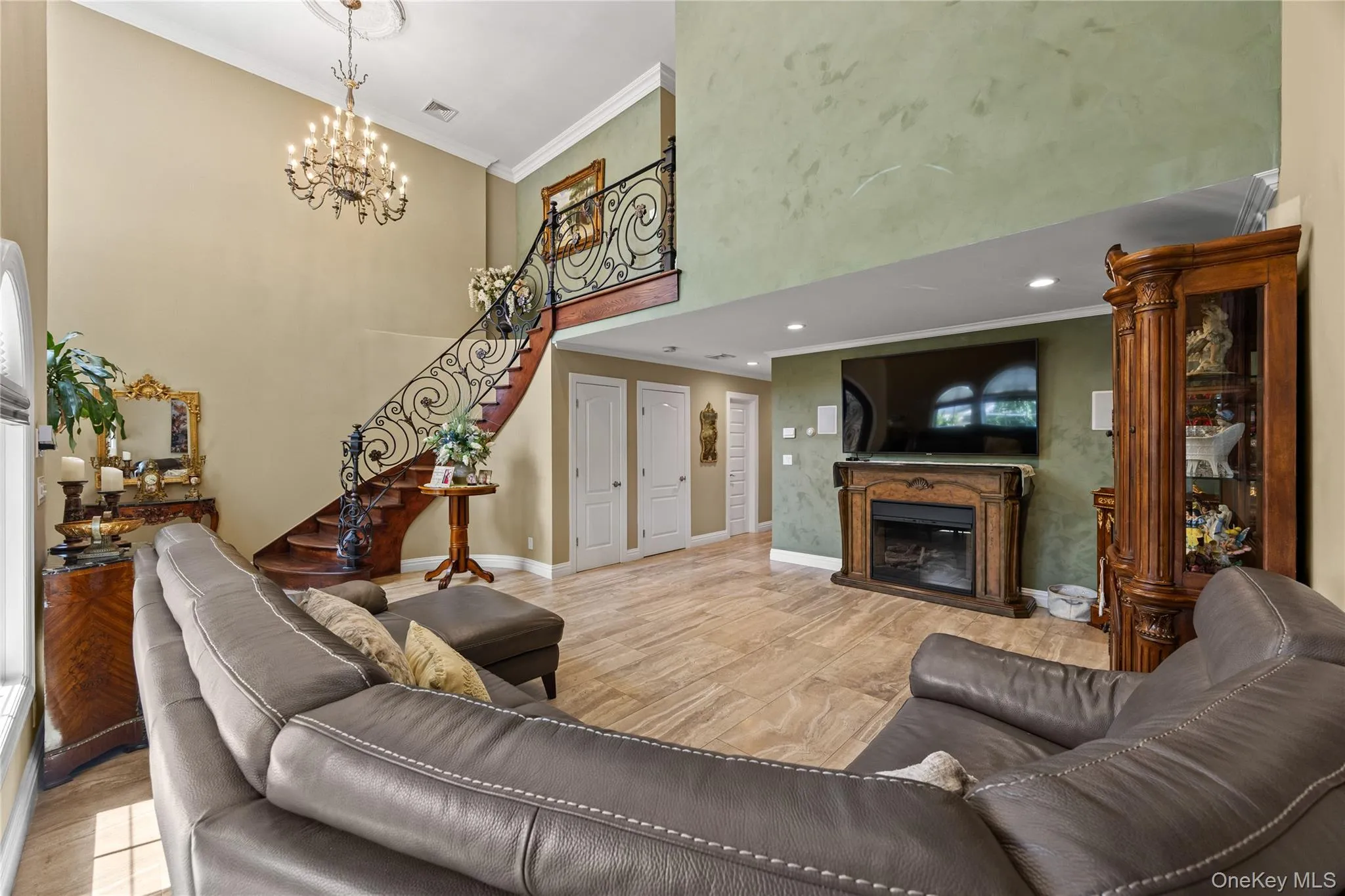 Two-story living area featuring a grand staircase with ornate wrought iron railing, a decorative chandelier, and recessed lighting Two-story living area featuring a grand staircase with ornate wrought iron railing, a decorative chandelier, and recessed lighting