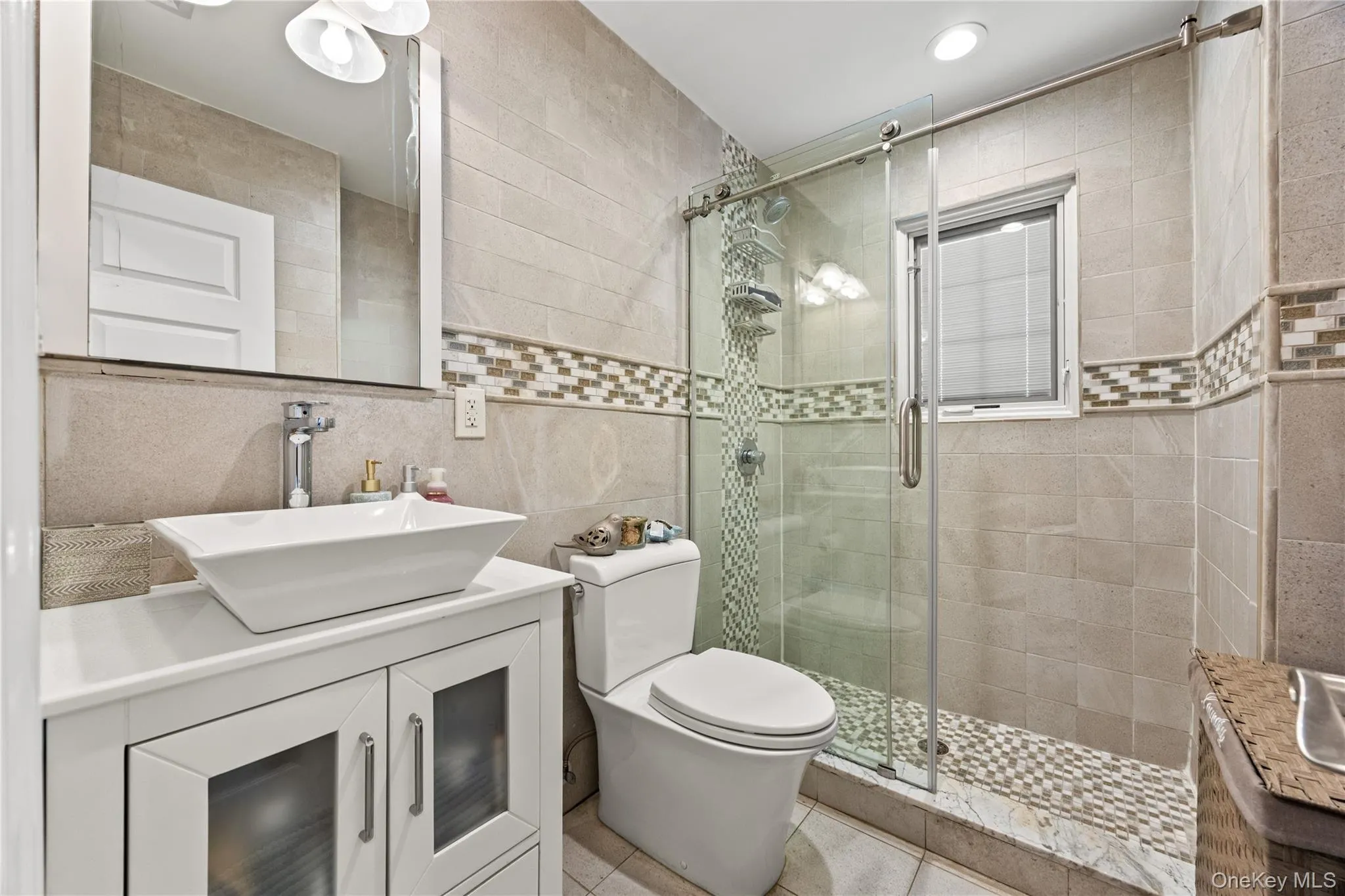 Bathroom featuring a glass-enclosed shower with mosaic tile details, a white floating vanity with vessel sink, and an integrated window Bathroom featuring a glass-enclosed shower with mosaic tile details, a white floating vanity with vessel sink, and an integrated window