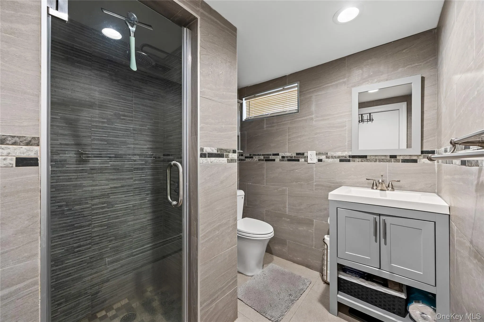 Fully tiled bathroom featuring a glass-enclosed shower with textured wall tile and a mosaic tile band Fully tiled bathroom featuring a glass-enclosed shower with textured wall tile and a mosaic tile band