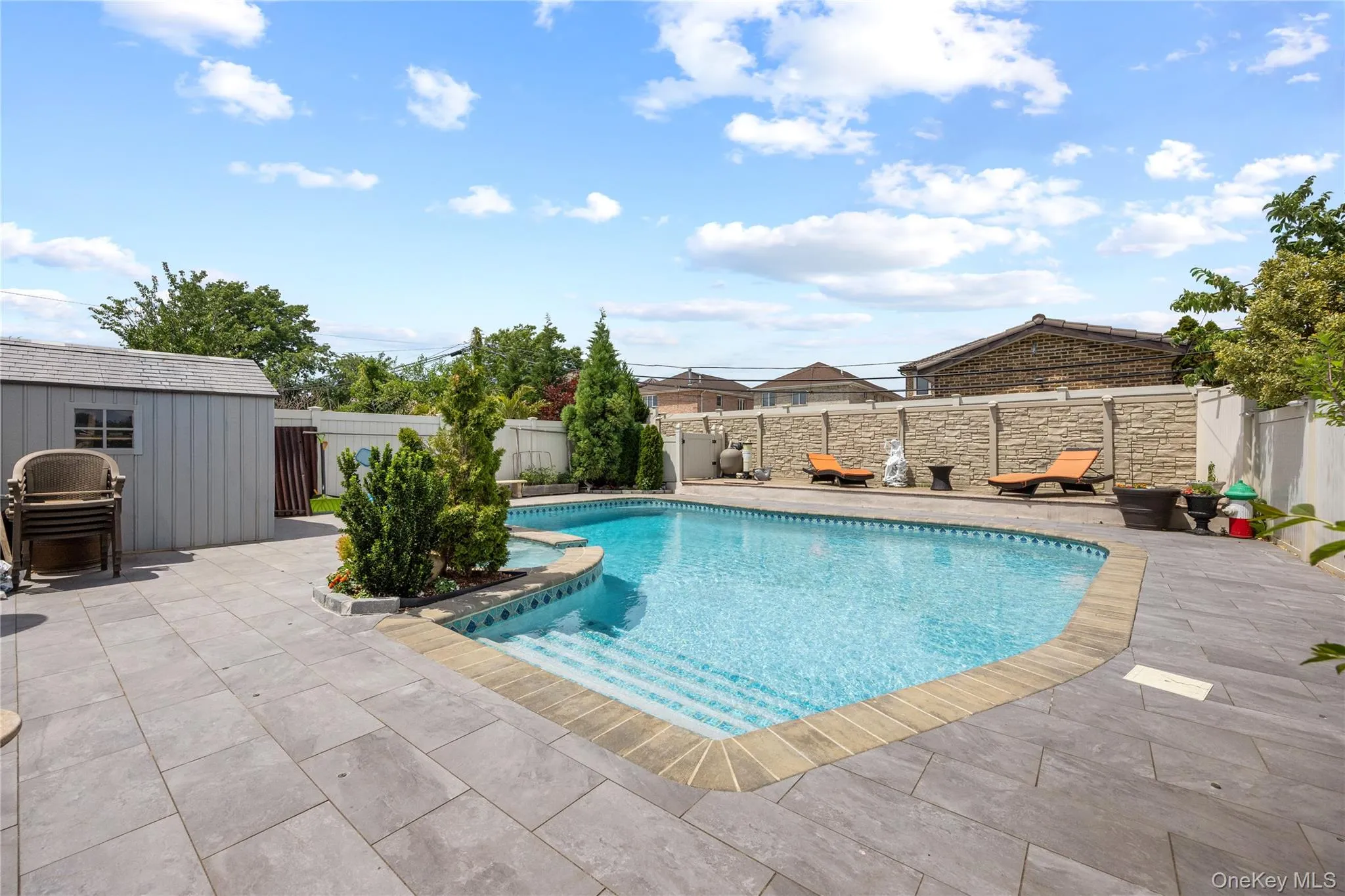 Outdoor pool area featuring a free-form swimming pool, extensive paver patio, stone-finish privacy wall, and dedicated storage shed Outdoor pool area featuring a free-form swimming pool, extensive paver patio, stone-finish privacy wall, and dedicated storage shed