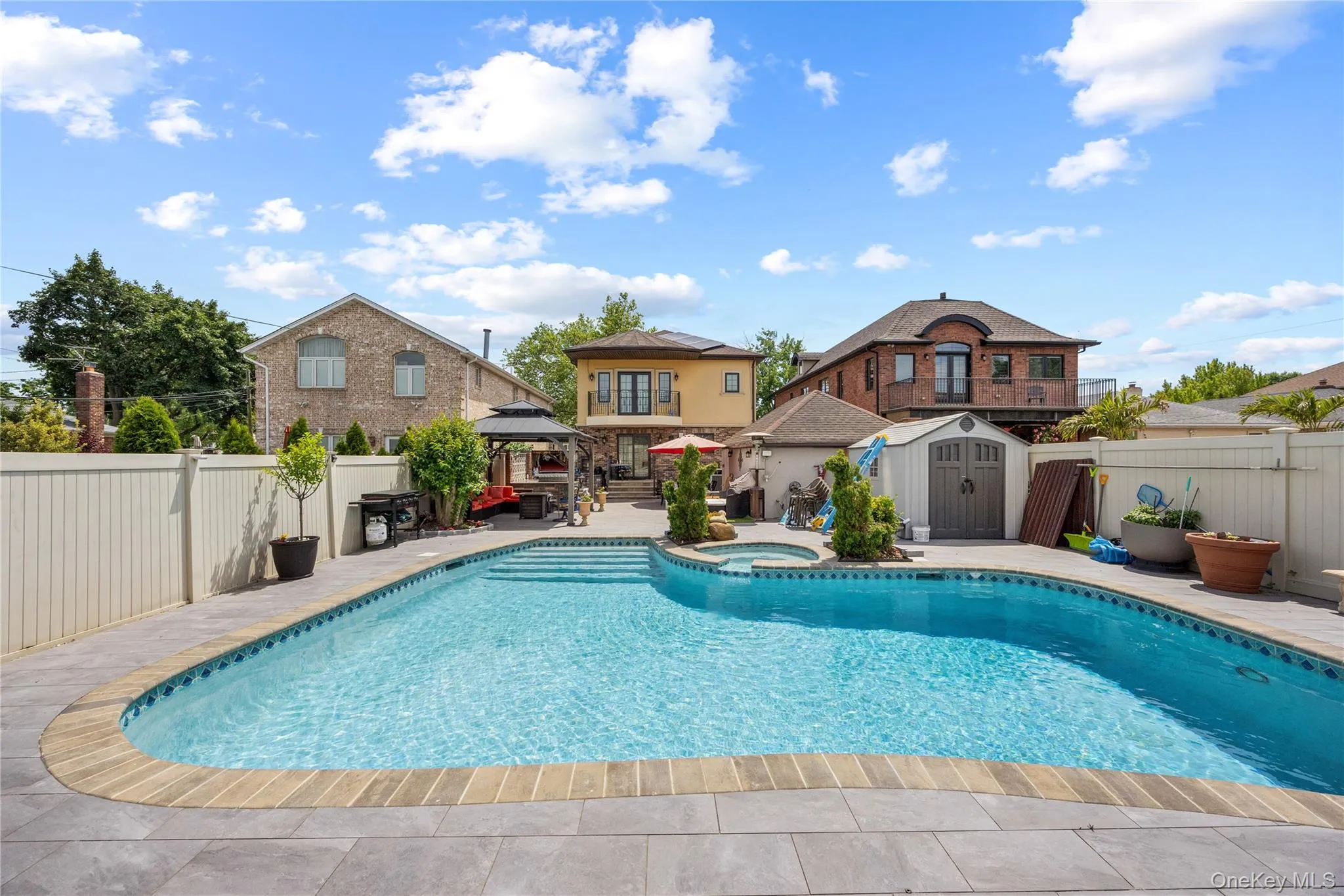 Expansive backyard featuring a large in-ground swimming pool with integrated steps, surrounded by light gray patio pavers Expansive backyard featuring a large in-ground swimming pool with integrated steps, surrounded by light gray patio pavers