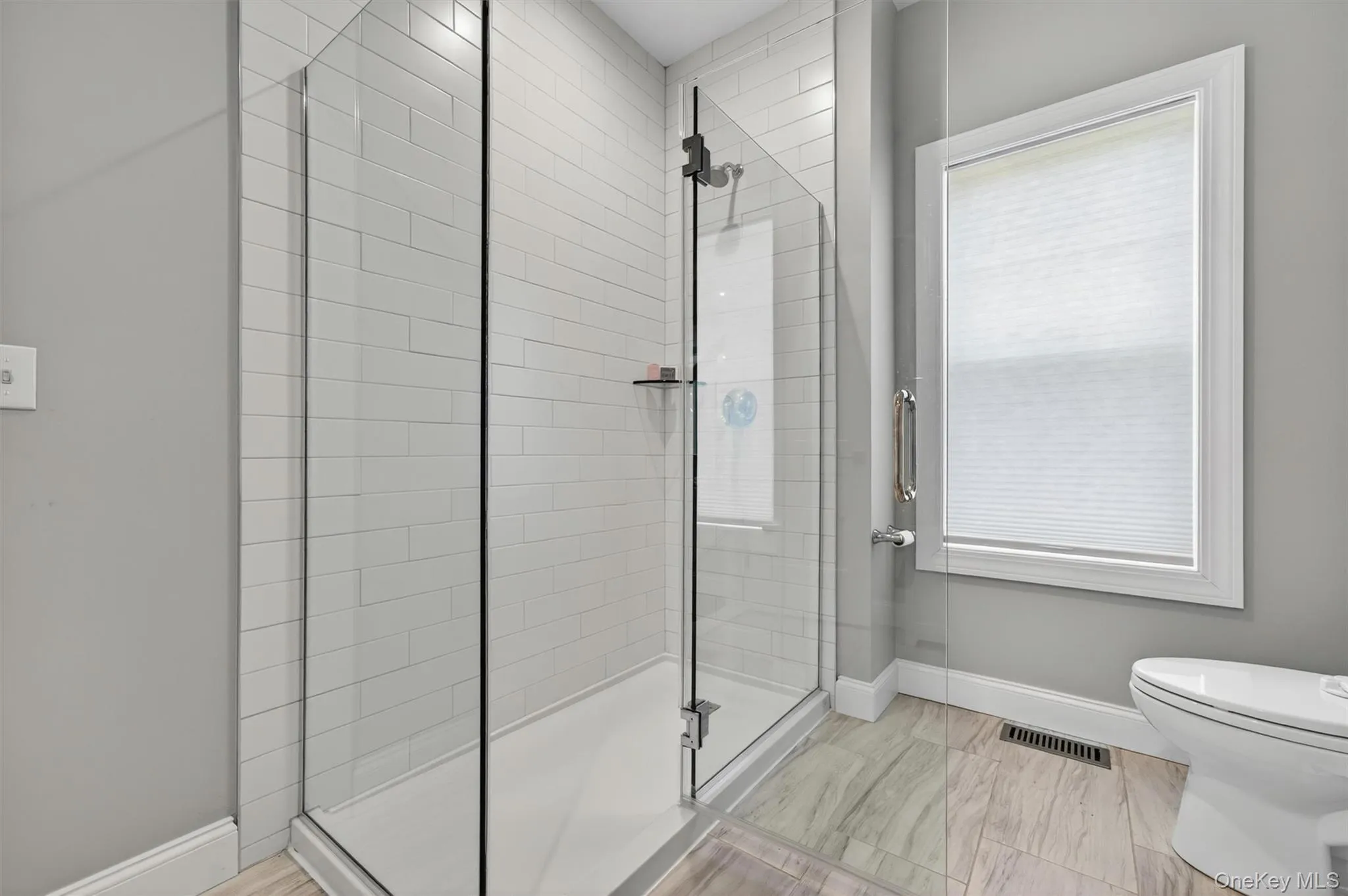 Glass-enclosed shower with white subway tile surround, integrated shower shelf, and a white base Glass-enclosed shower with white subway tile surround, integrated shower shelf, and a white base