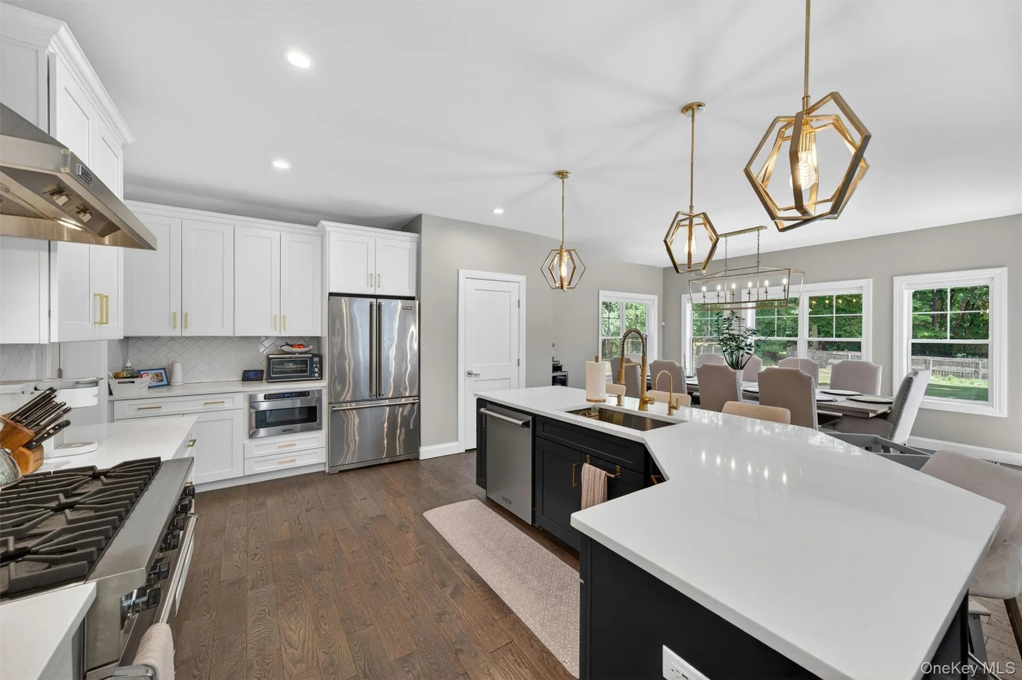 Open-concept kitchen featuring white shaker cabinetry, stainless steel appliances, and a central island with a sink and breakfast bar Open-concept kitchen featuring white shaker cabinetry, stainless steel appliances, and a central island with a sink and breakfast bar