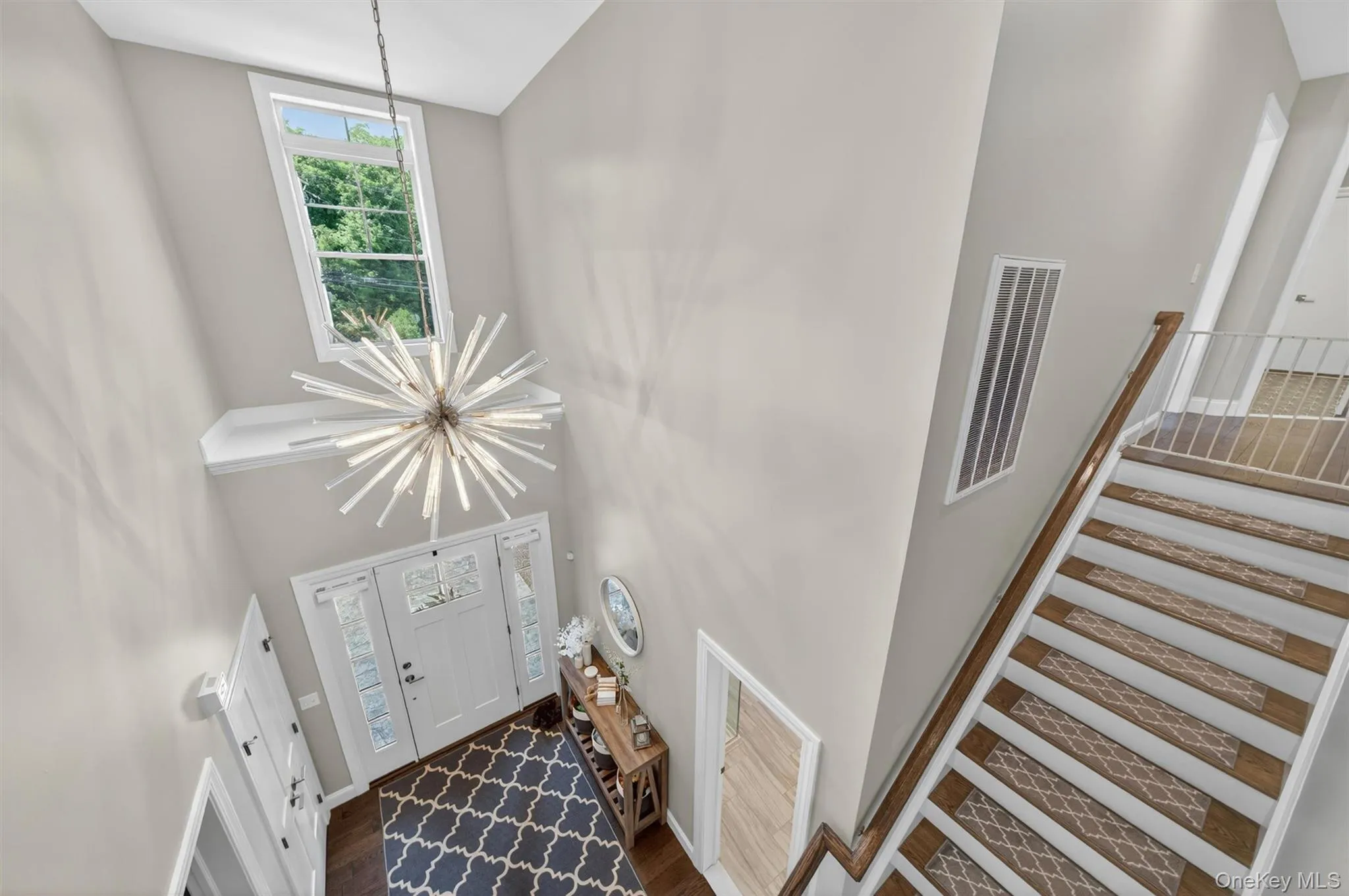 Two-story foyer featuring a starburst chandelier, transom windows, hardwood flooring, and a staircase with wood-finish handrails Two-story foyer featuring a starburst chandelier, transom windows, hardwood flooring, and a staircase with wood-finish handrails