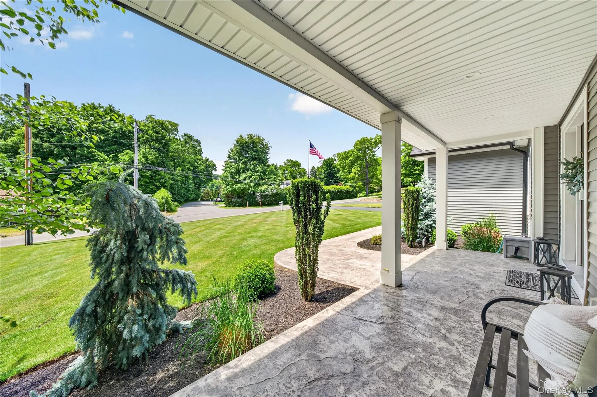 Covered porch with textured concrete flooring, white columns, and wood-look siding Covered porch with textured concrete flooring, white columns, and wood-look siding