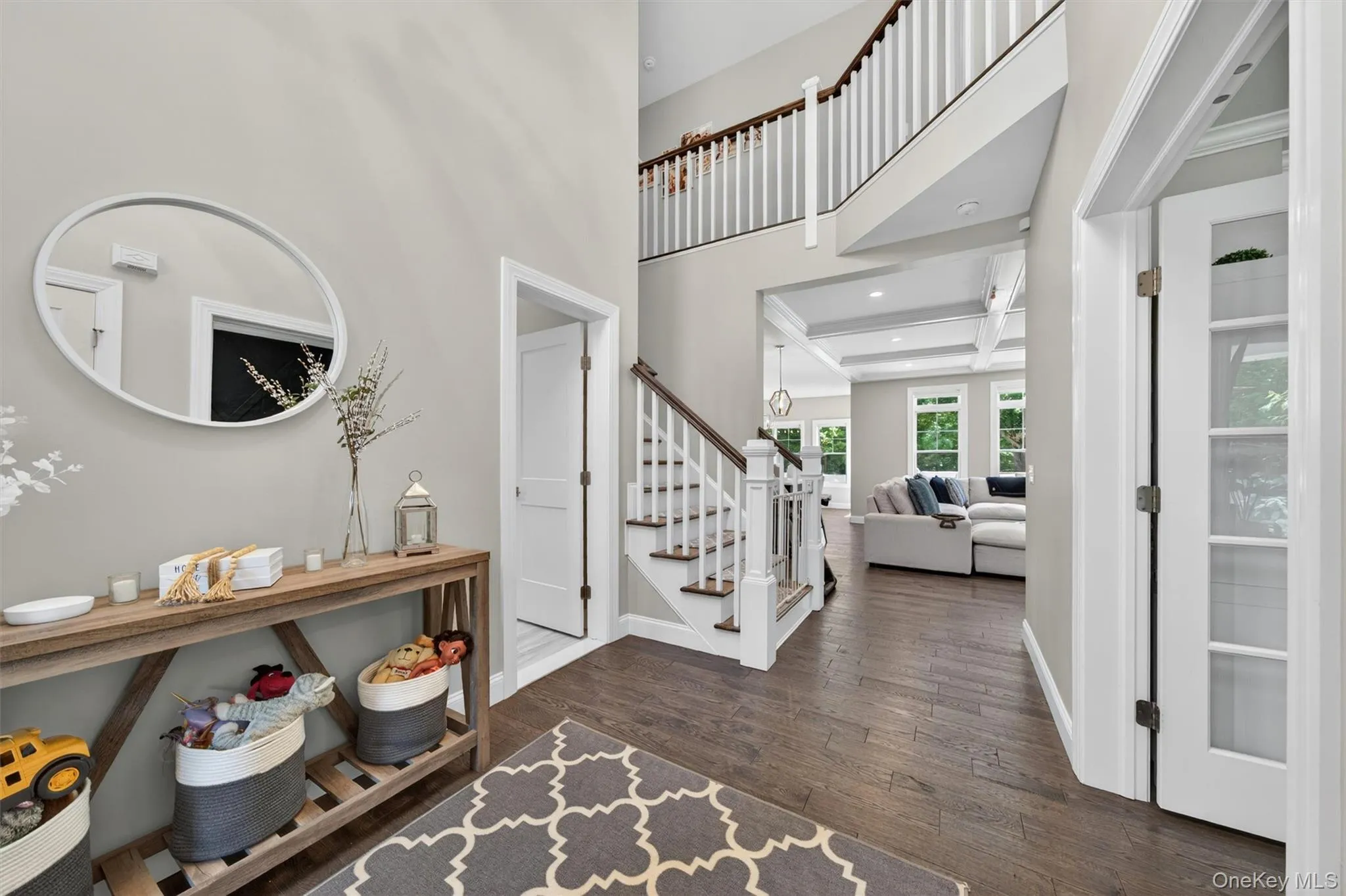 Two-story foyer featuring wood-finish flooring, white staircase with dark wood handrail, and an upper-level balcony Two-story foyer featuring wood-finish flooring, white staircase with dark wood handrail, and an upper-level balcony