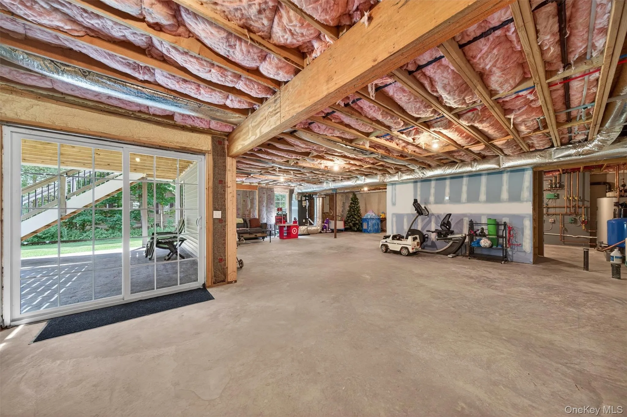 Spacious unfinished basement featuring exposed wood beams, concrete flooring, and a large glass sliding door leading to an outdoor patio Spacious unfinished basement featuring exposed wood beams, concrete flooring, and a large glass sliding door leading to an outdoor patio