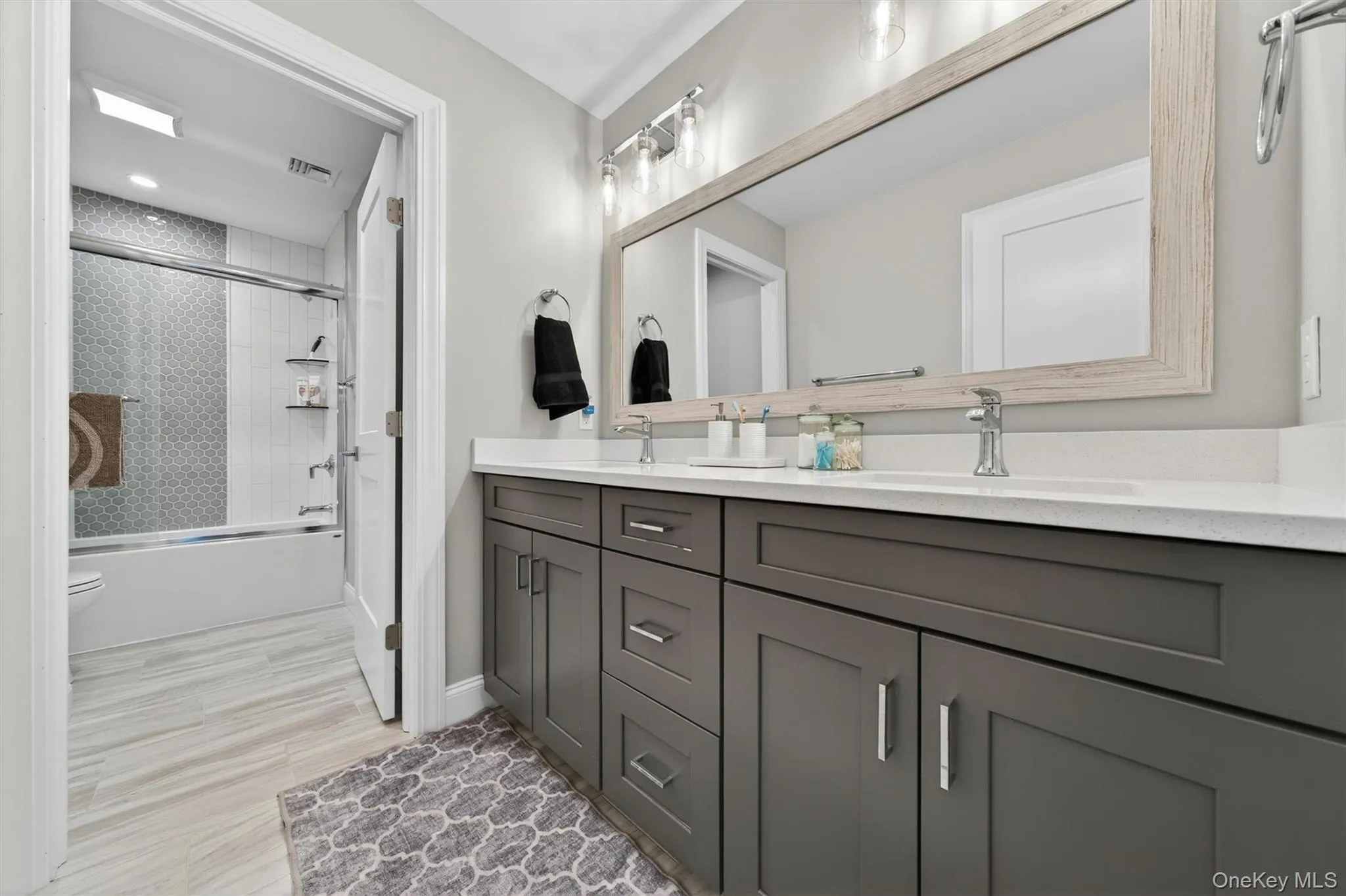 Double vanity with white countertop, chrome fixtures, and a large framed mirror Double vanity with white countertop, chrome fixtures, and a large framed mirror