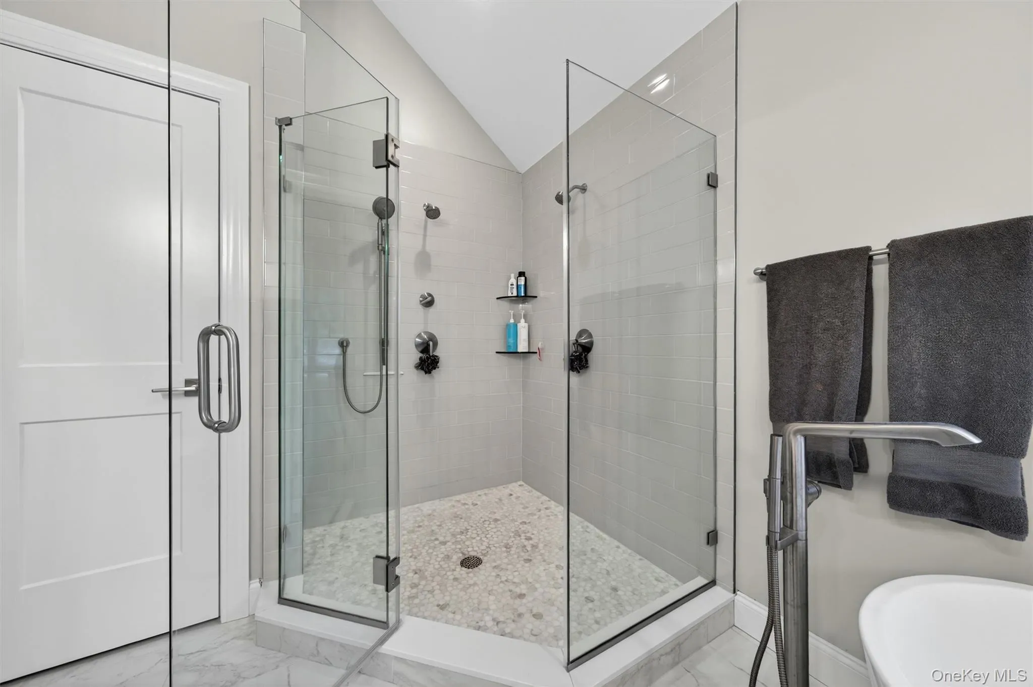 Spacious walk-in shower featuring dual shower heads and a pebble-tiled floor Spacious walk-in shower featuring dual shower heads and a pebble-tiled floor