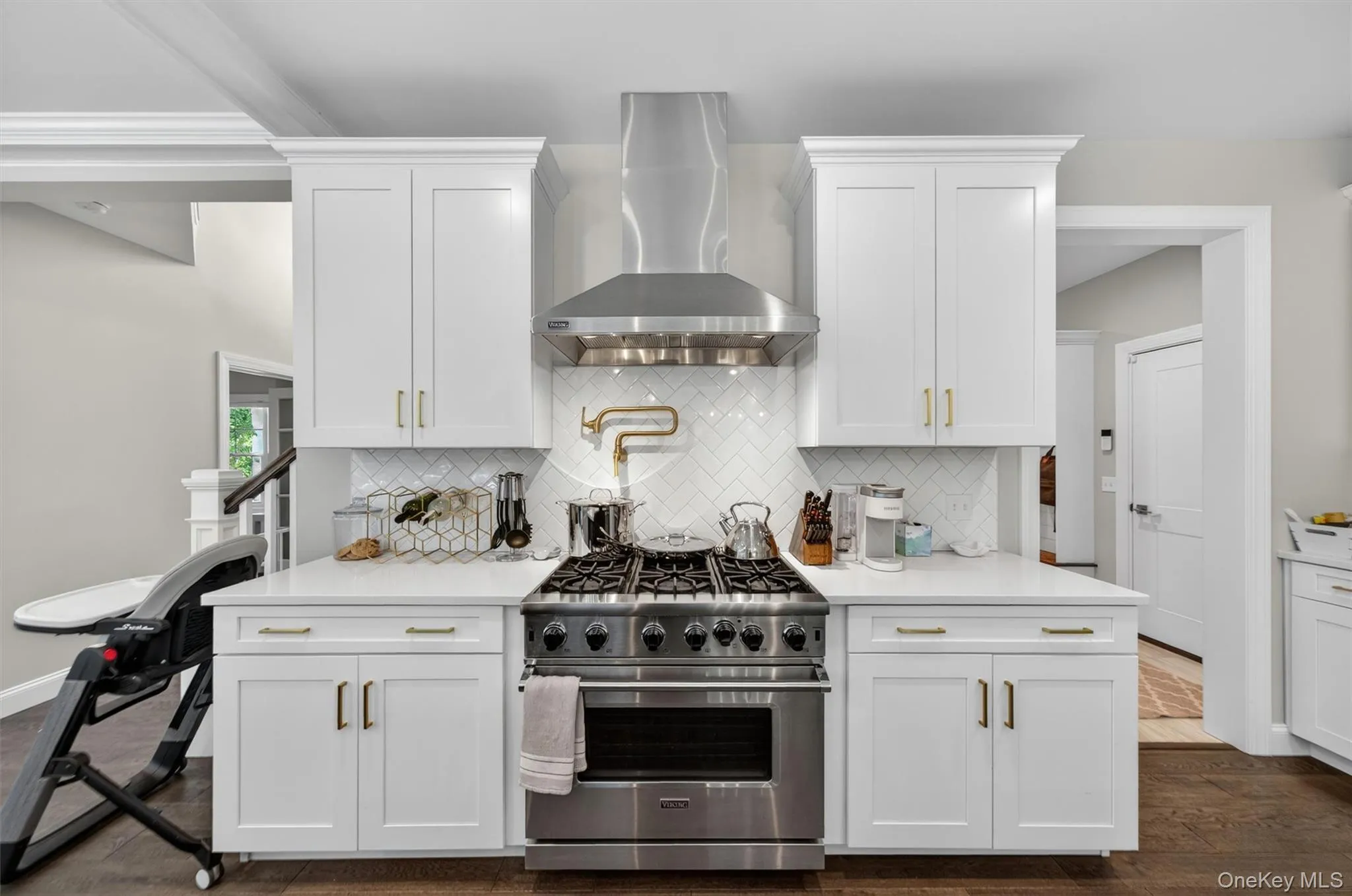 Gourmet kitchen featuring a stainless steel gas range with a matching range hood, white shaker cabinetry, an intricate white tile backsplash, and light-toned countertops Gourmet kitchen featuring a stainless steel gas range with a matching range hood, white shaker cabinetry, an intricate white tile backsplash, and light-toned countertops