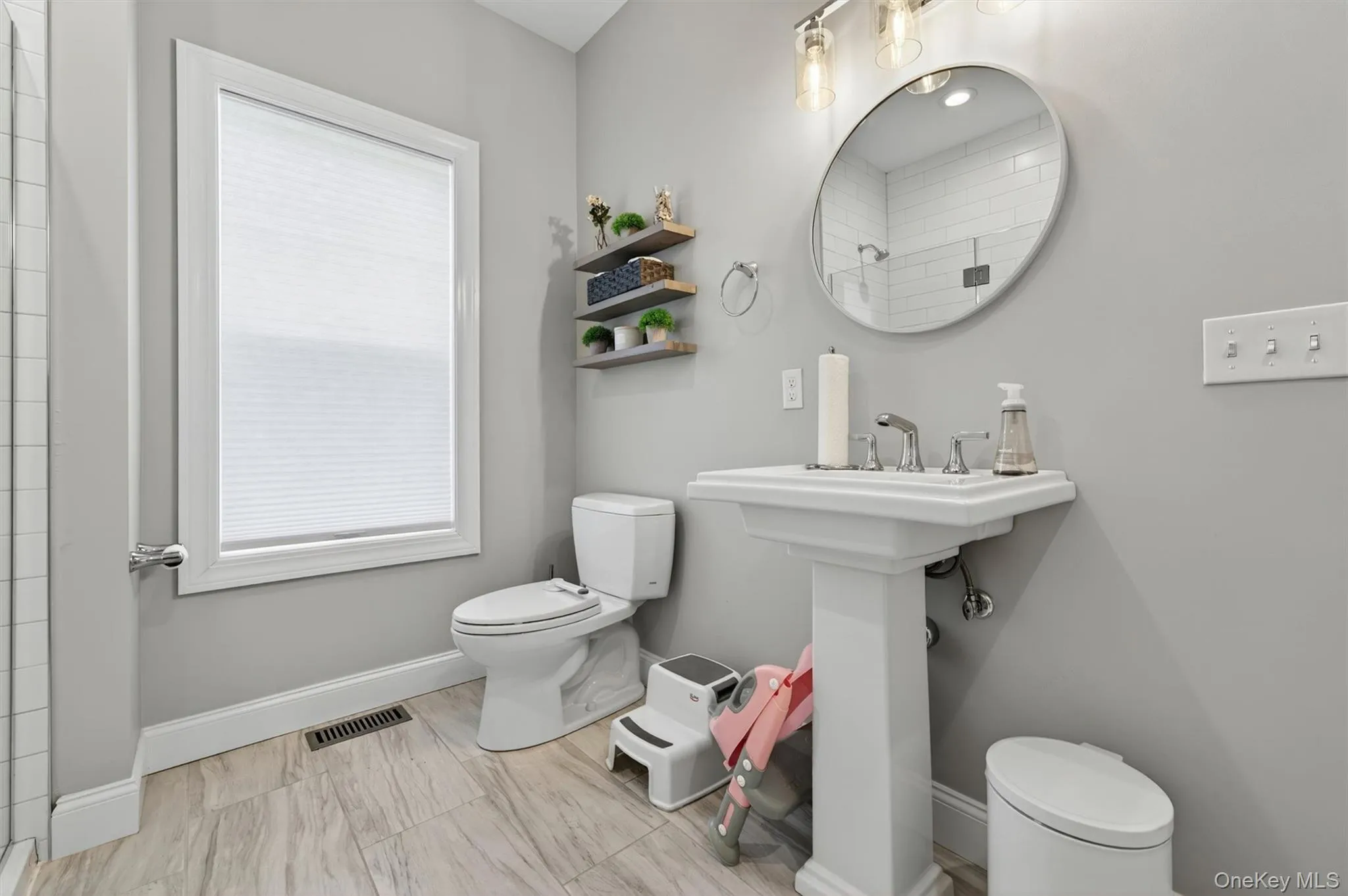Bathroom featuring a pedestal sink, round mirror, and wood-finish tile flooring Bathroom featuring a pedestal sink, round mirror, and wood-finish tile flooring