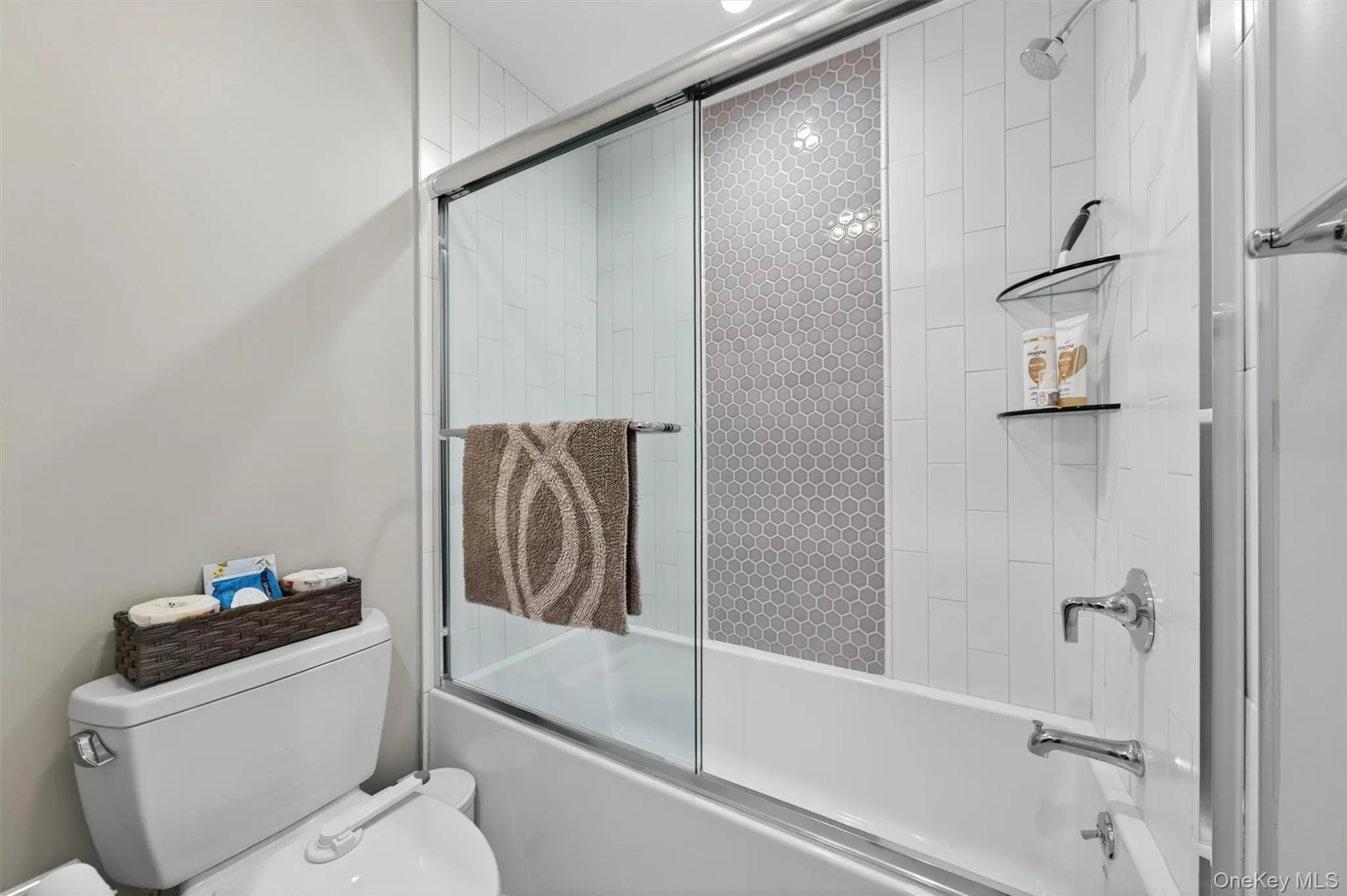 Bathtub with sliding glass shower door, chrome fixtures, and a white subway tile surround featuring a hexagonal mosaic accent band Bathtub with sliding glass shower door, chrome fixtures, and a white subway tile surround featuring a hexagonal mosaic accent band