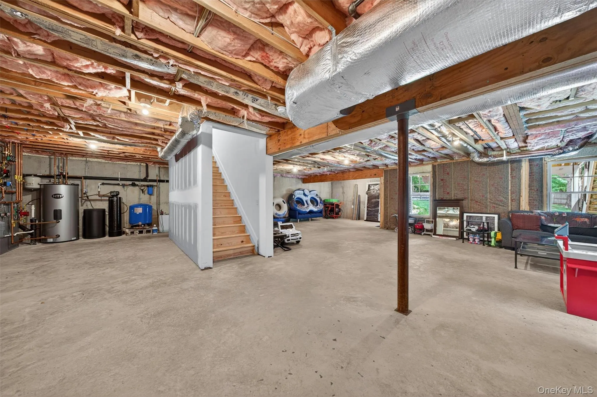 Expansive basement featuring exposed ceiling joists, concrete flooring, a finished staircase, and visible utility systems Expansive basement featuring exposed ceiling joists, concrete flooring, a finished staircase, and visible utility systems
