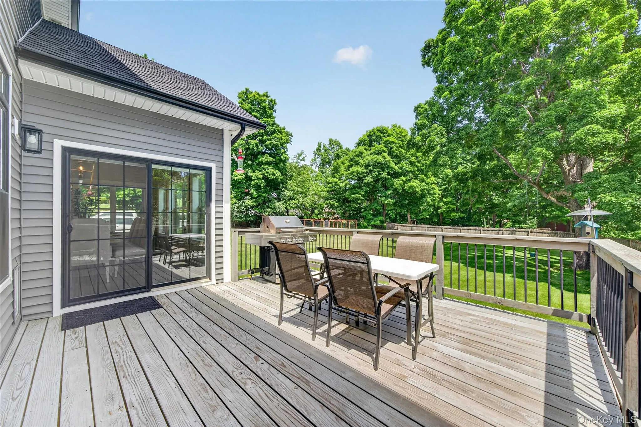 Expansive wood-finish deck featuring dark railings, a sliding glass door with grid detailing, and a exterior wall sconce Expansive wood-finish deck featuring dark railings, a sliding glass door with grid detailing, and a exterior wall sconce