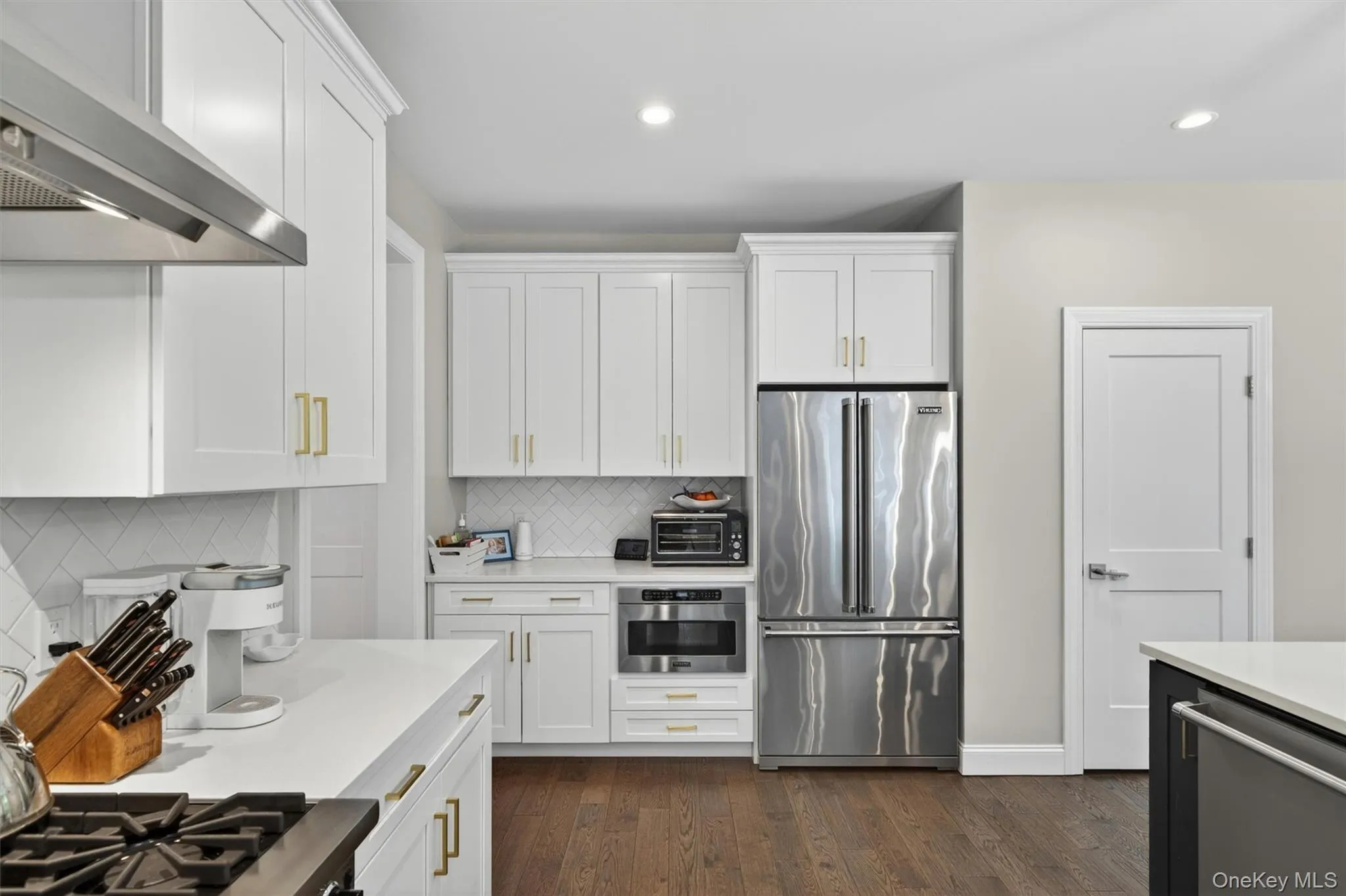 Kitchen featuring white shaker cabinetry with gold-tone hardware, stainless steel appliances, and wood-finish flooring Kitchen featuring white shaker cabinetry with gold-tone hardware, stainless steel appliances, and wood-finish flooring