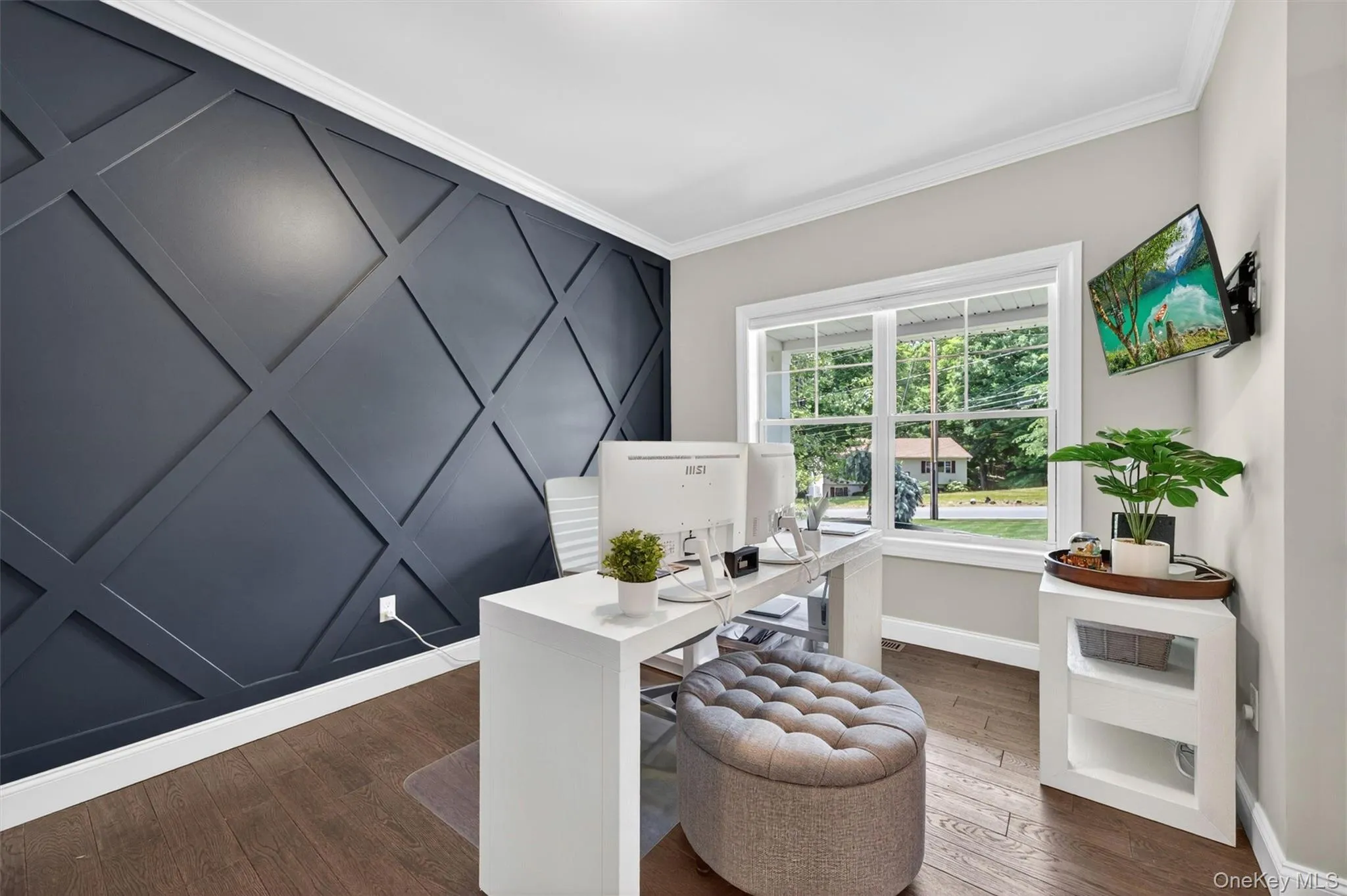 Accent wall featuring geometric paneling, wood-finish flooring, white crown molding, a large window, and light-toned wall paint Accent wall featuring geometric paneling, wood-finish flooring, white crown molding, a large window, and light-toned wall paint