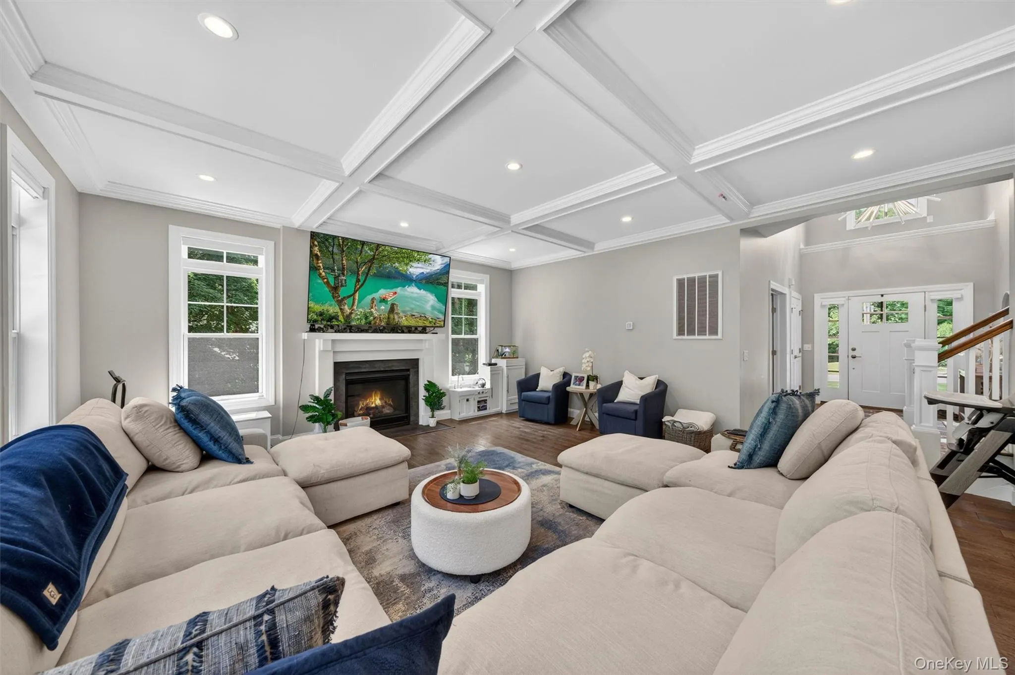 Spacious living area featuring coffered ceilings, recessed lighting, a fireplace with a mantel, large windows, and wood-finish flooring Spacious living area featuring coffered ceilings, recessed lighting, a fireplace with a mantel, large windows, and wood-finish flooring